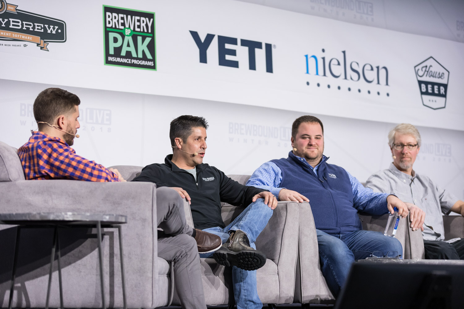 Four men on gray couches on stage in front of Brewery Pak, YETI and Nielsen logos.