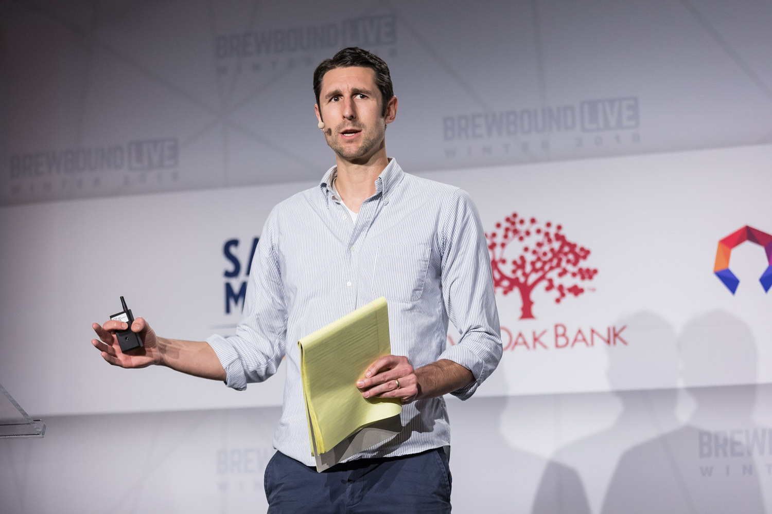 A man in a light button-up shirt holds a yellow legal pad and a clicker in front of a Live Oak Bank logo.