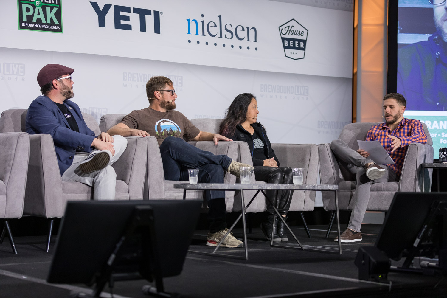 Four people on gray stage couches in front of Brewery Pak, YETI and Nielsen logos.
