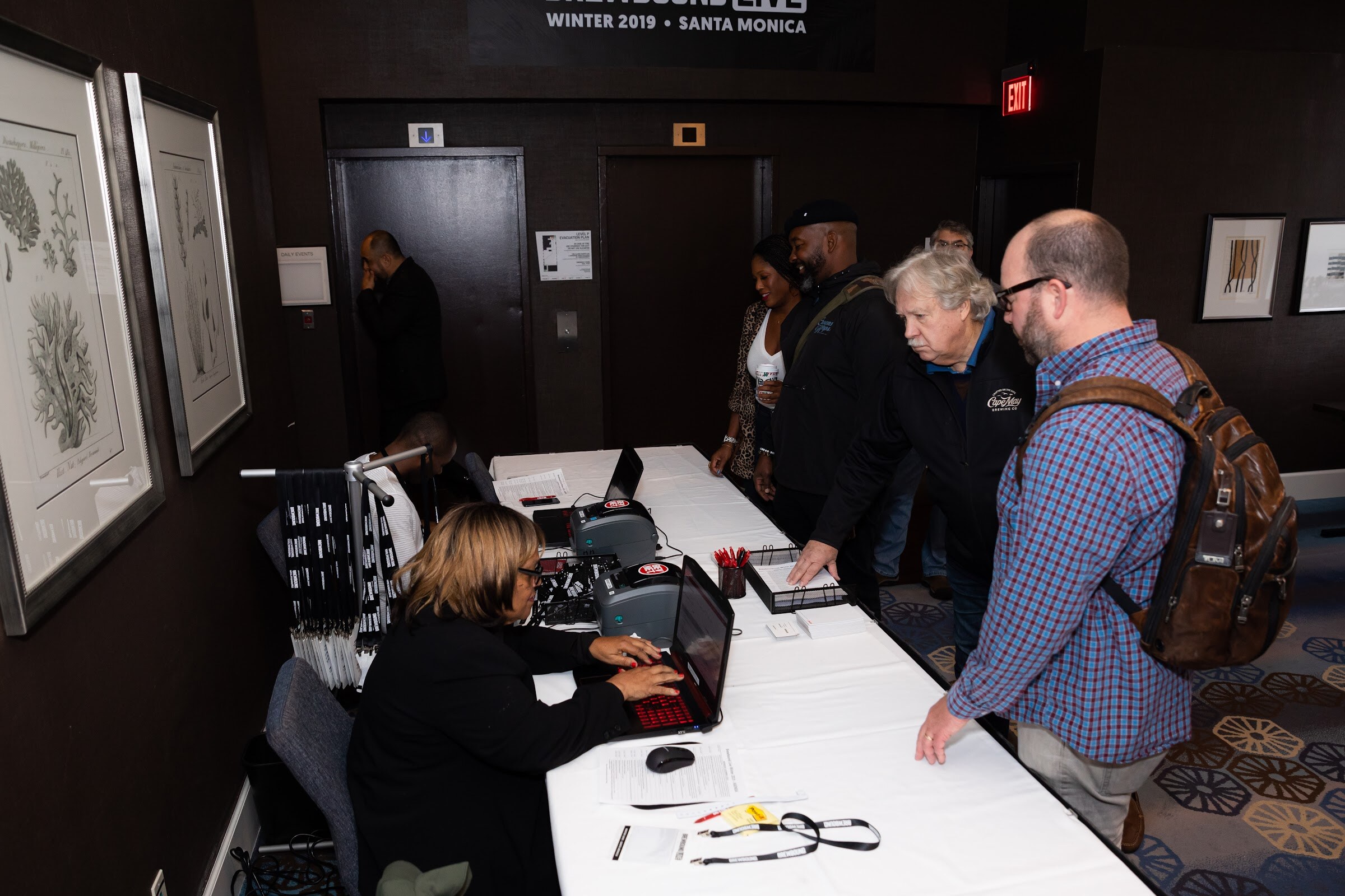 Woman at a registration table with a laptop checking in several attendees, under a Brewbound Live Winter 2019 Santa Monica sign.