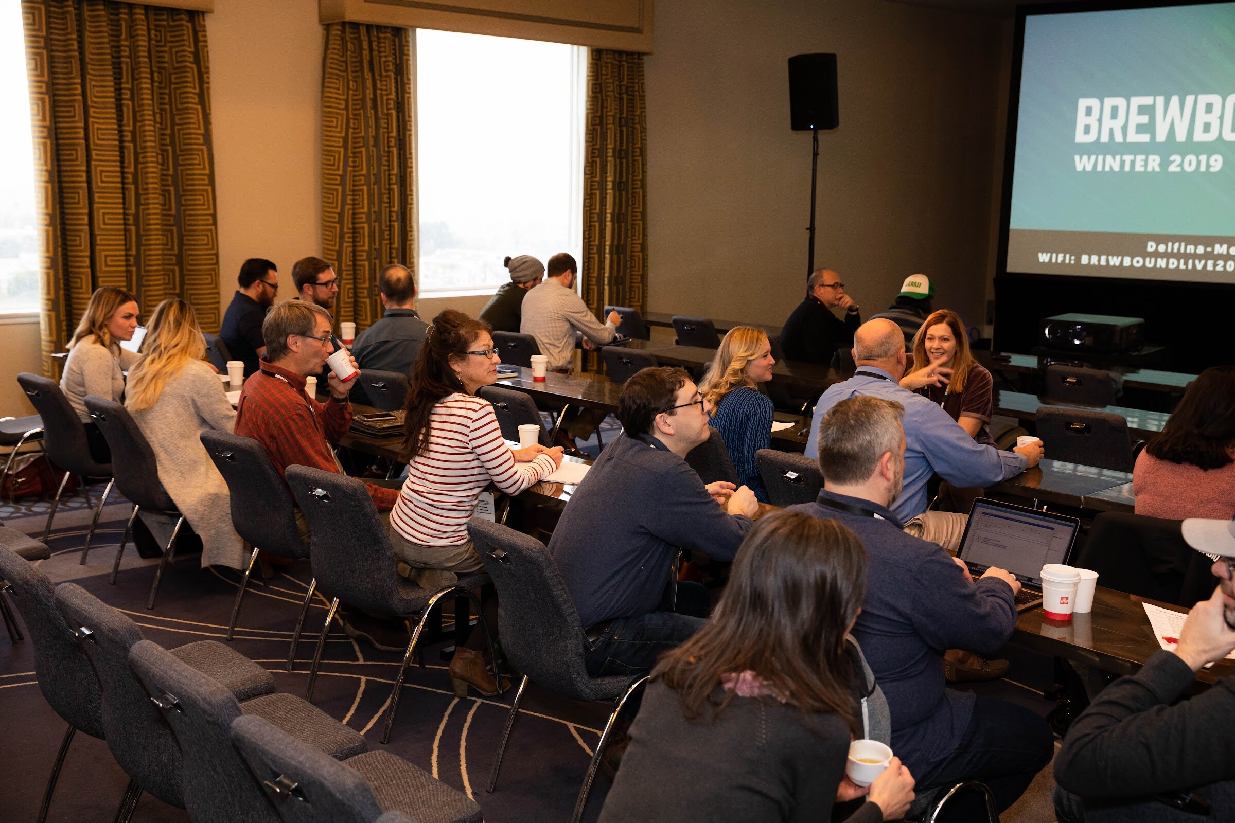 Rows of attendees seated at tables in a meeting room with a screen reading Brewbound Winter 2019.