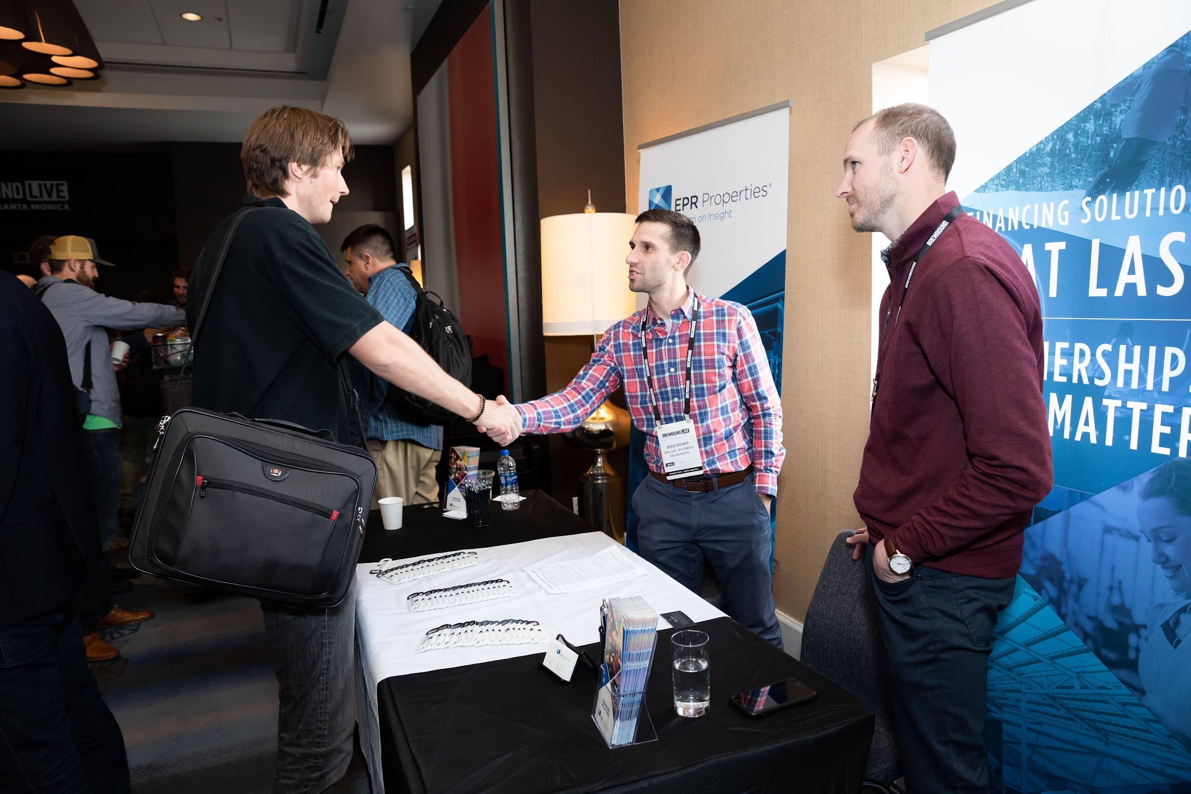 Two men shaking hands at a table with brochures in front of an EPR Properties banner.
