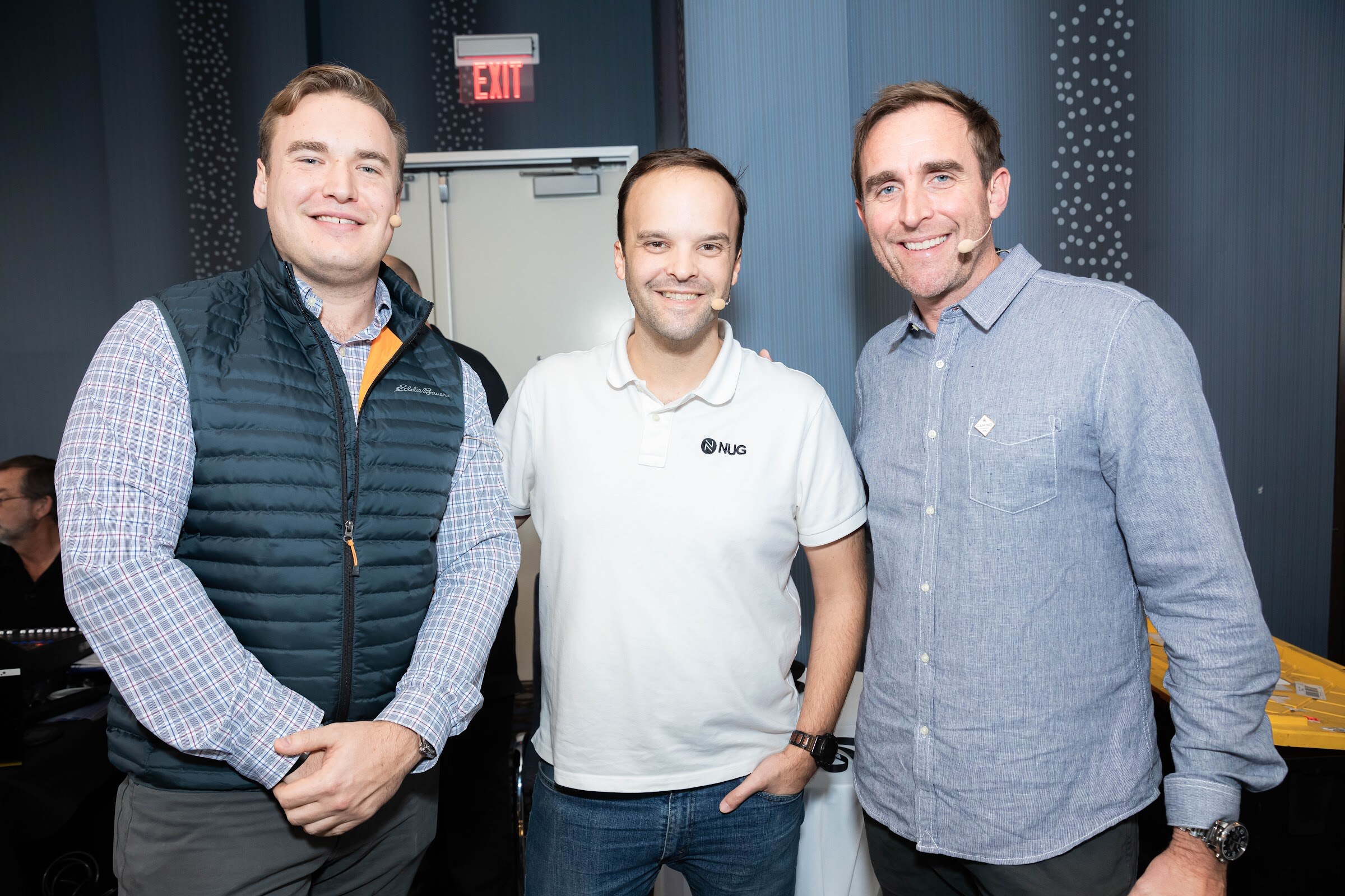 Three men standing side by side smiling; the center man wears a white NUG polo shirt.