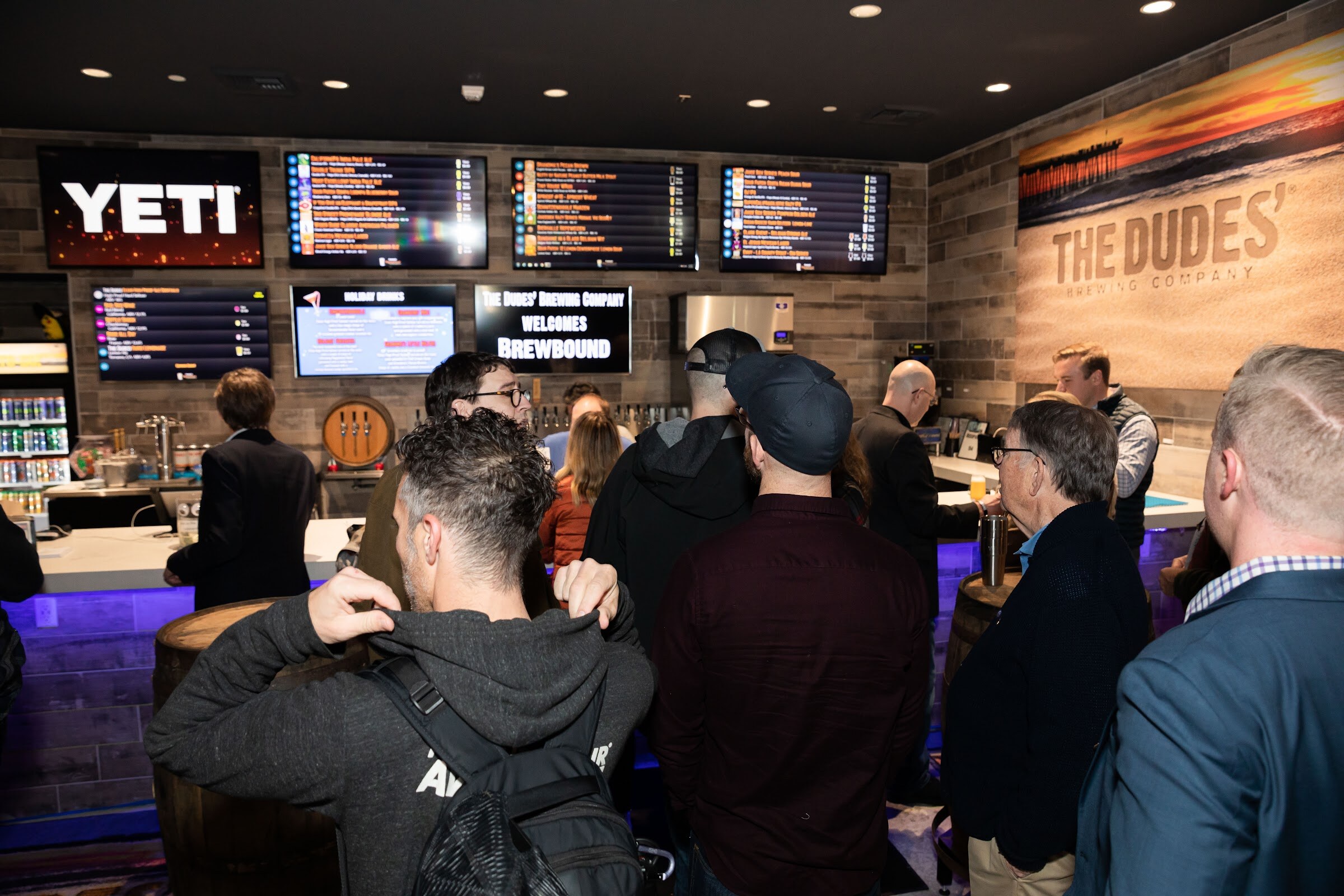 Crowded bar with YETI signage and screens including one reading The Dudes' Brewing Company Welcomes Brewbound.