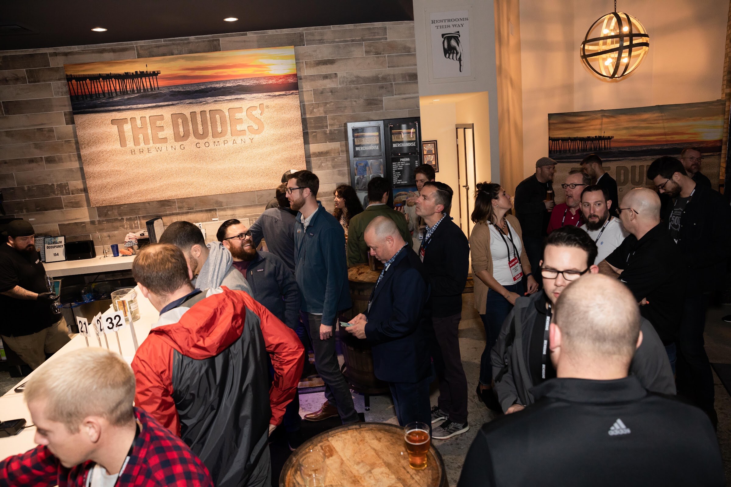 Wide shot of attendees talking in a brewery taproom with The Dudes' Brewing Company mural on the wall.