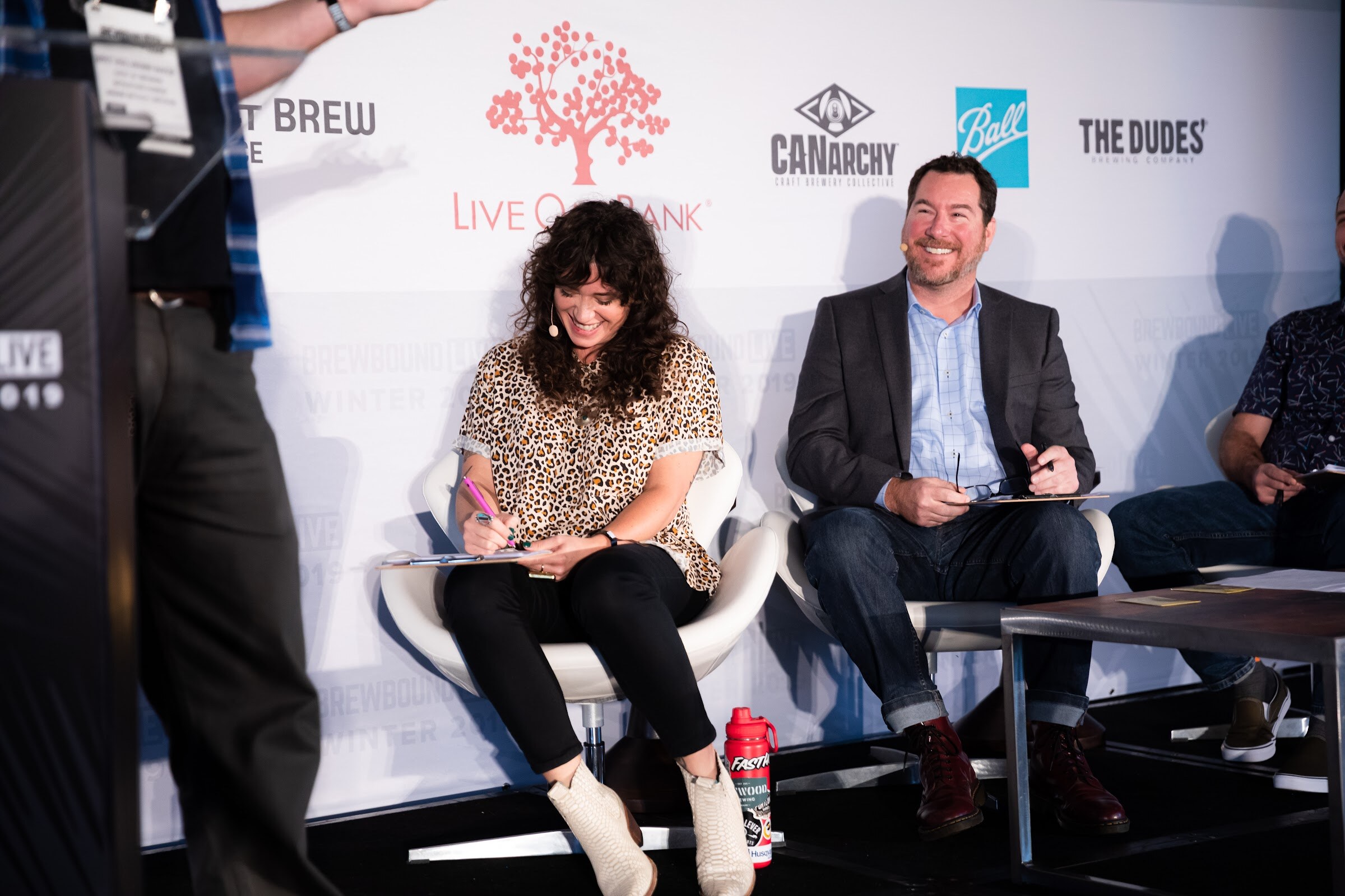 Woman in a leopard-print top writing on a clipboard next to a smiling man in a dark blazer.