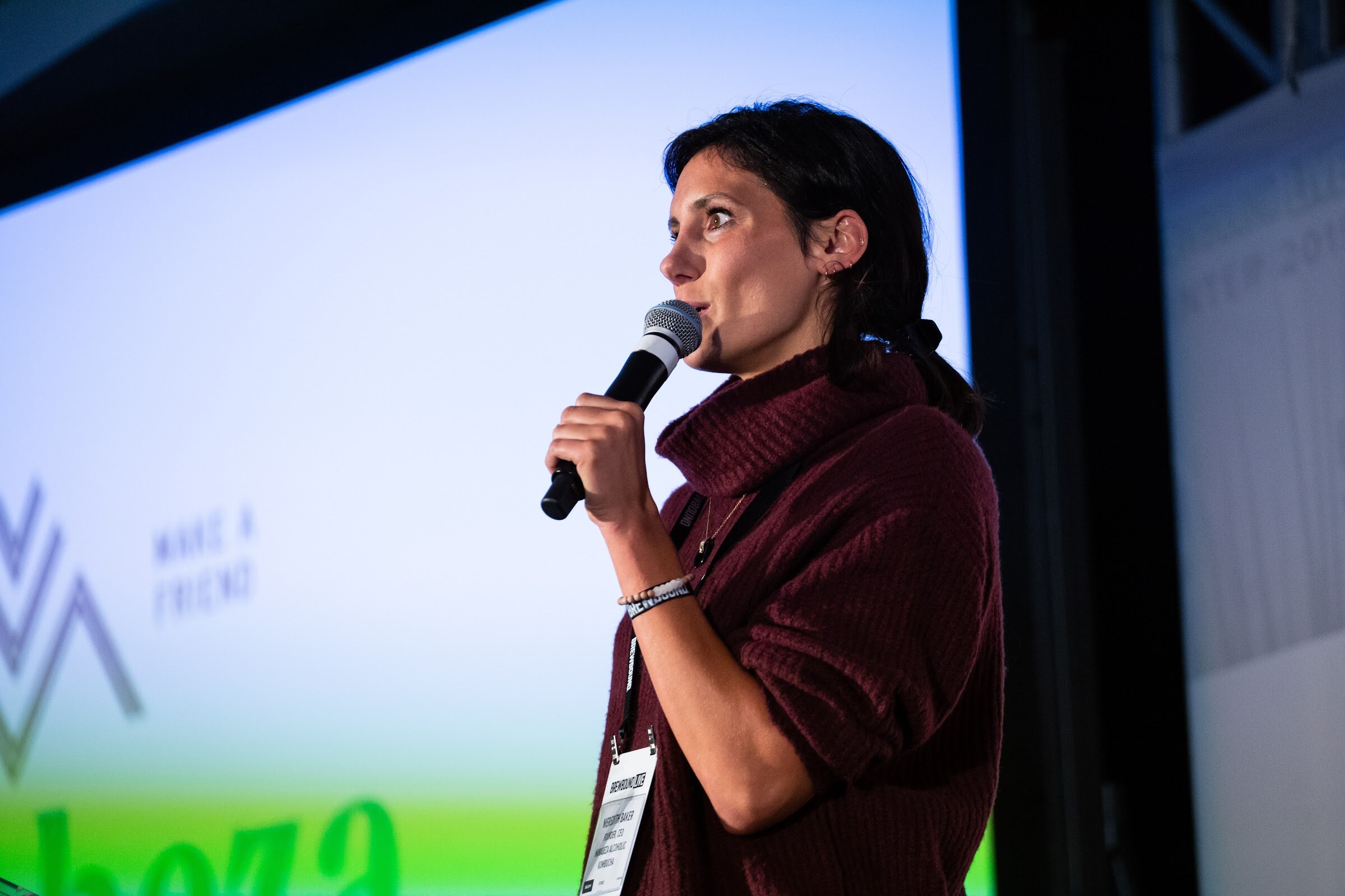 Dark-haired woman in a maroon sweater holding a microphone in front of a projected slide.