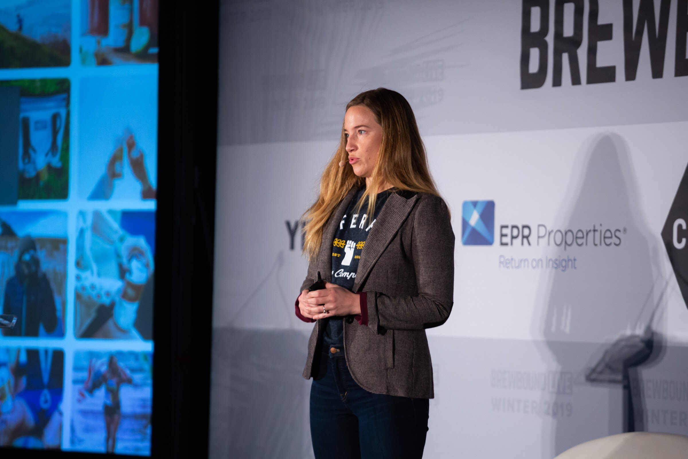 Woman in a tweed blazer standing on stage beside a screen showing a collage of lifestyle photos.