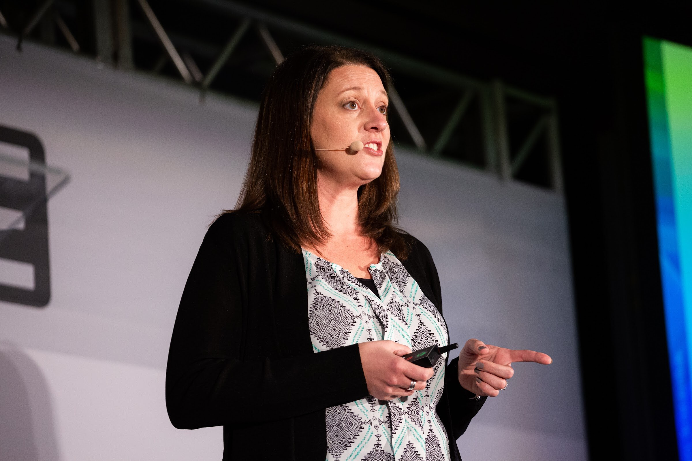 Woman in a black cardigan and patterned blouse pointing with one hand and holding a clicker.