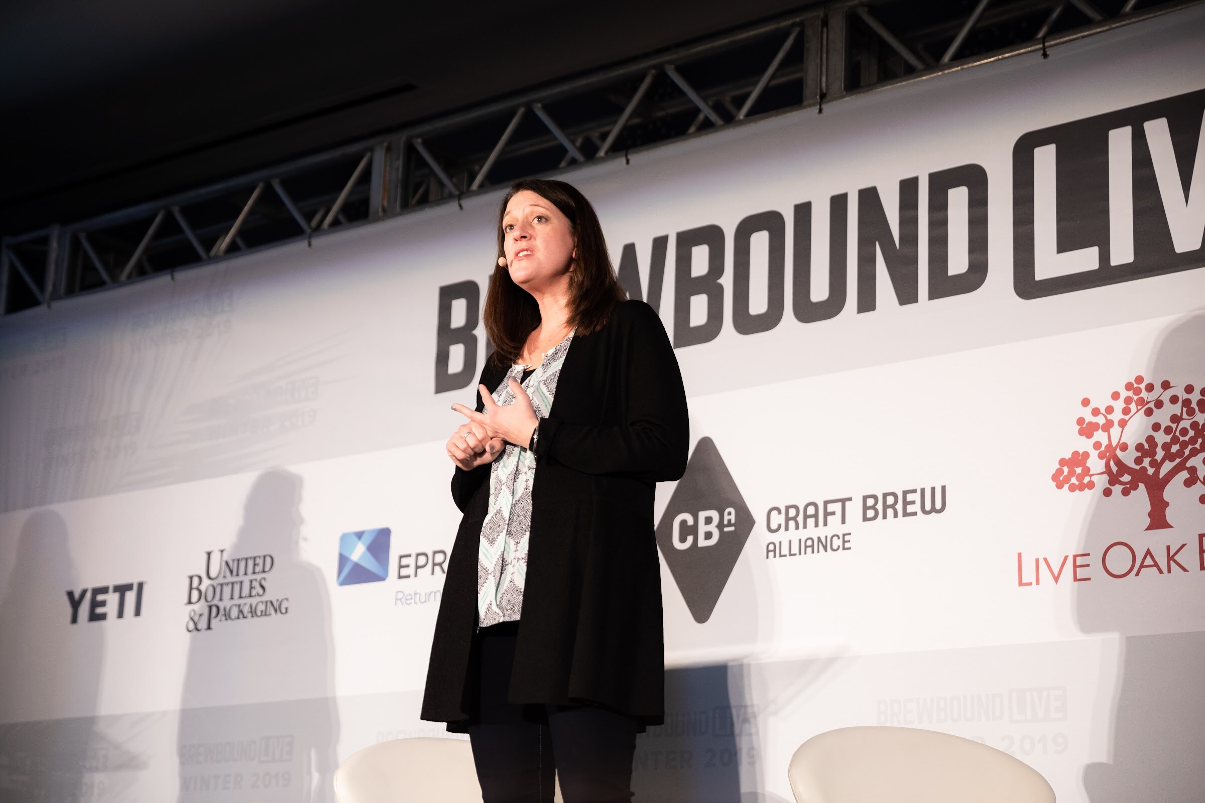 Woman in a black cardigan standing on stage in front of the Brewbound Live backdrop.