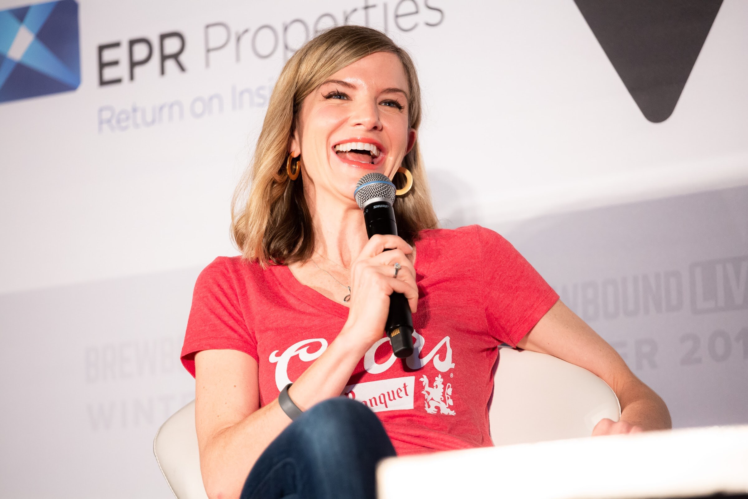 Woman in a red Coors Banquet T-shirt laughing while holding a microphone.