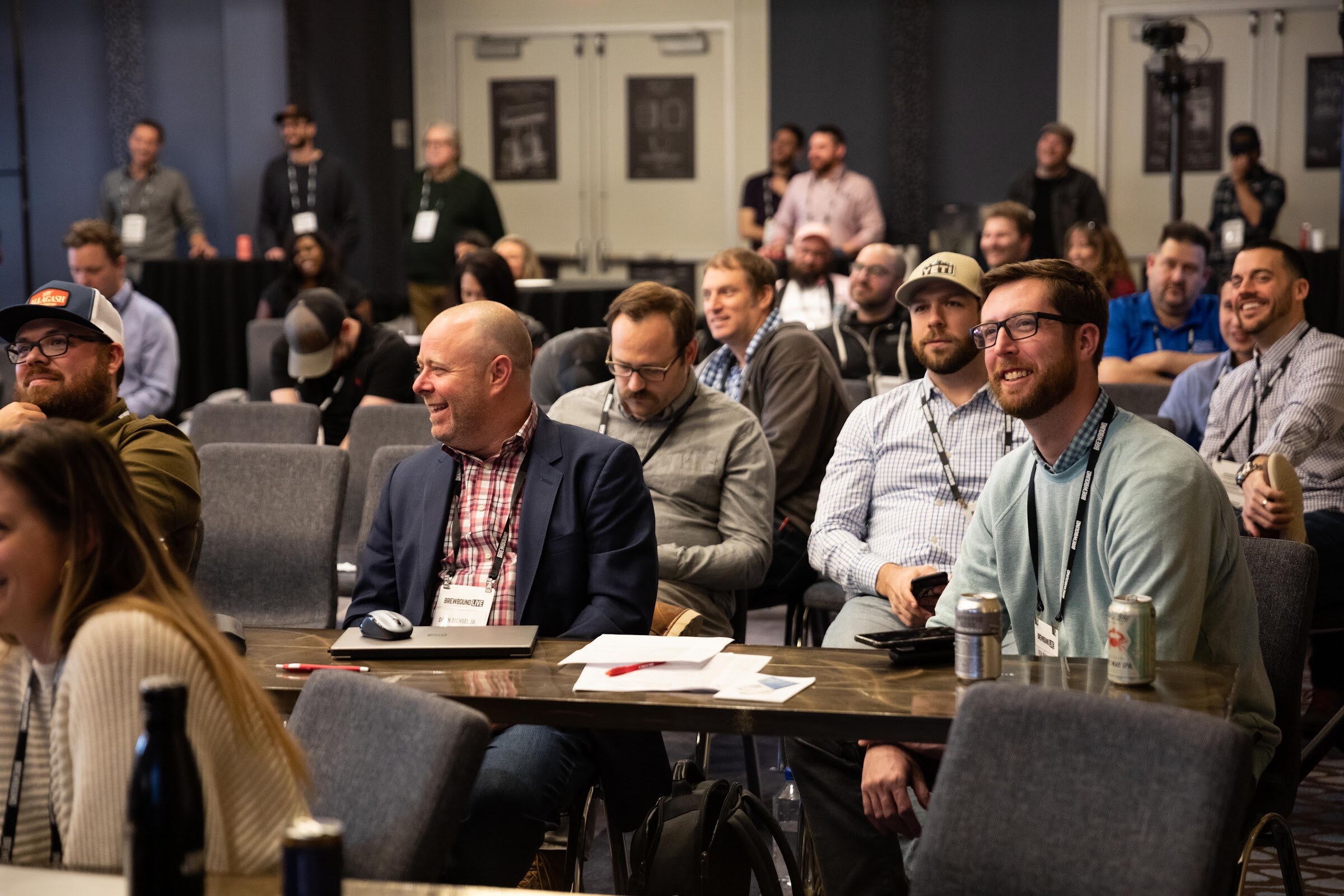 Seated attendees with badges and beer cans smiling and laughing at a conference table.