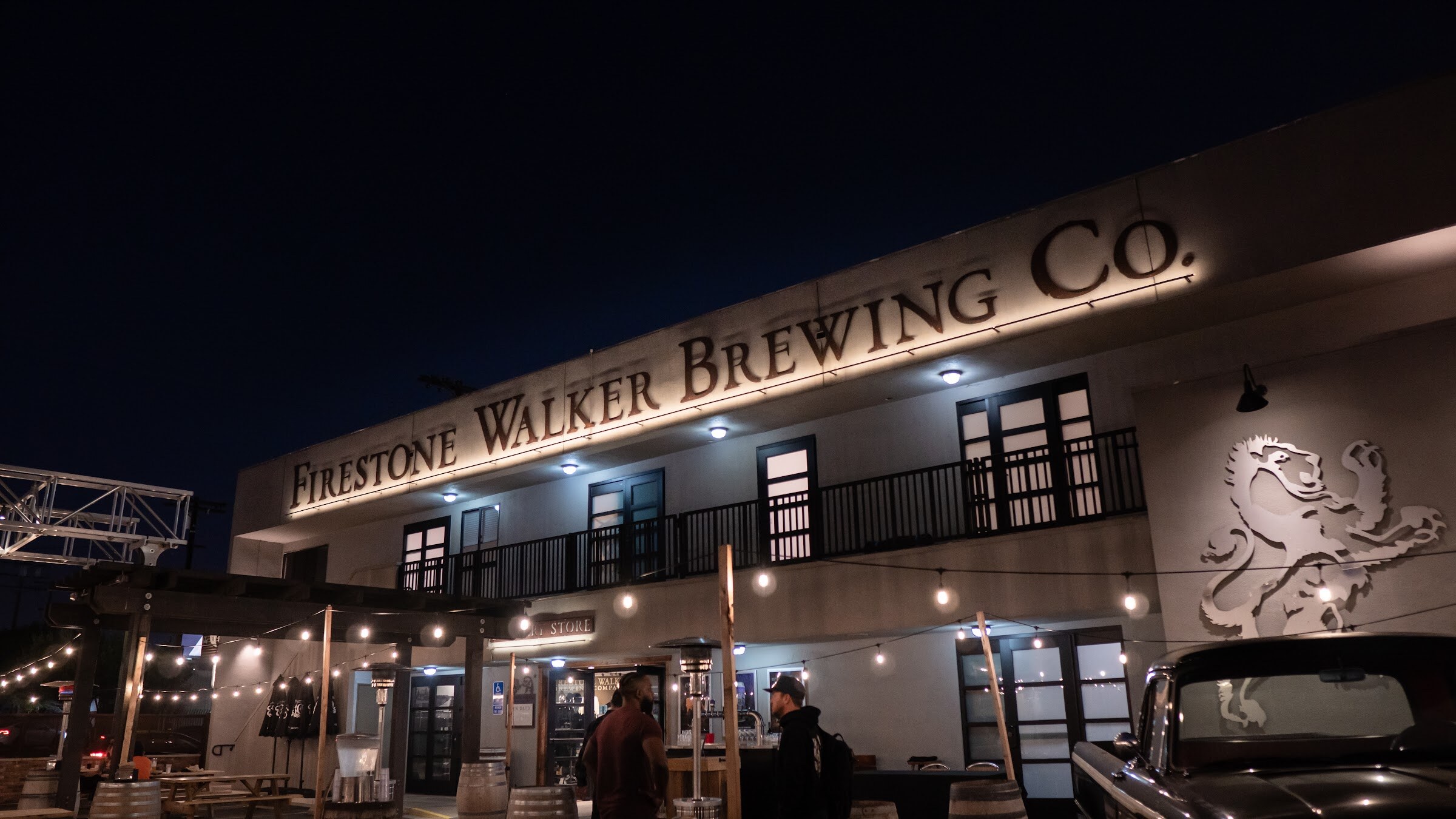 The exterior of a two-story building with a Firestone Walker Brewing Co. sign and lion logo at night, with string lights over the patio.