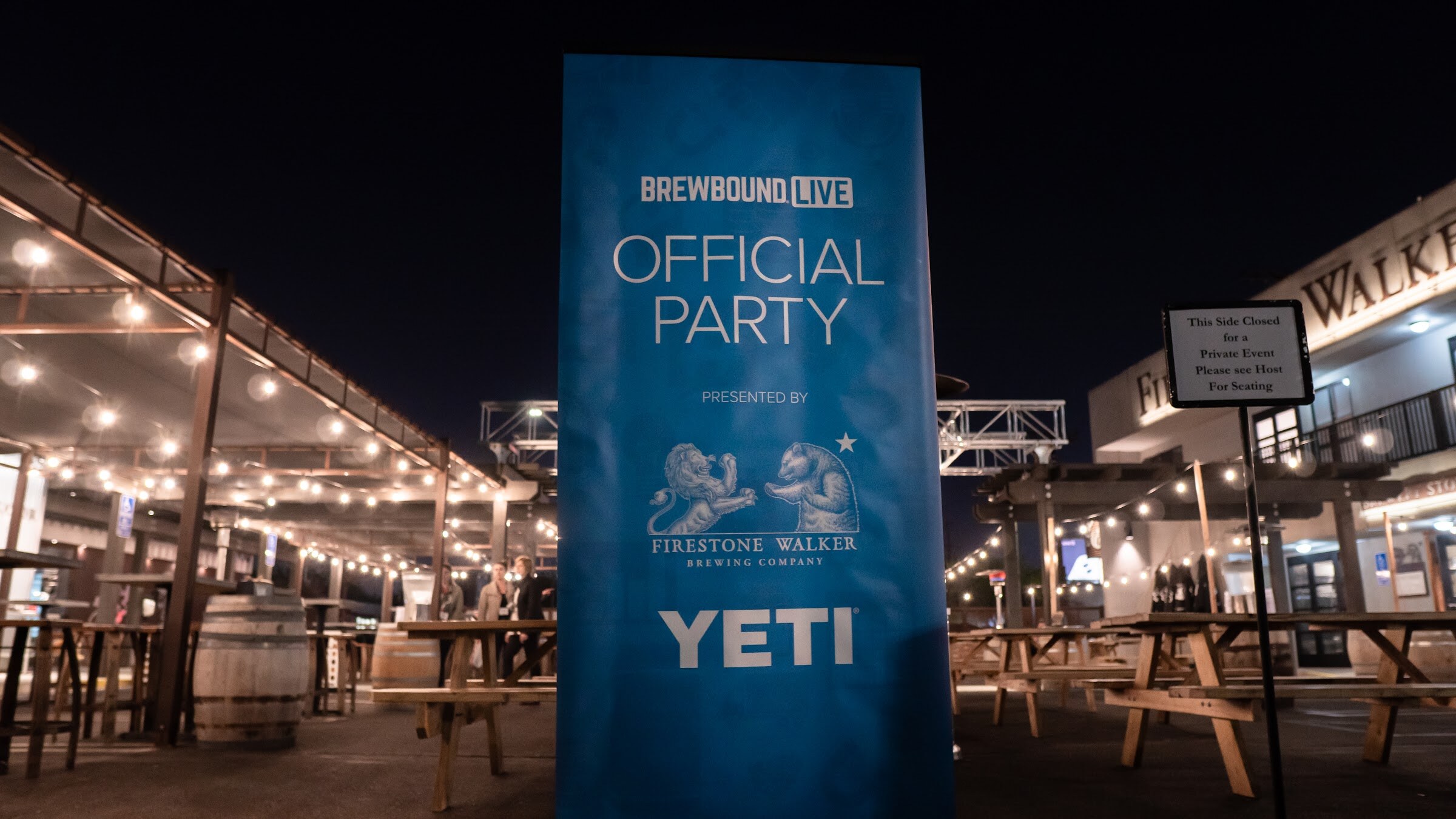 A tall blue banner reading Brewbound Live Official Party presented by Firestone Walker and YETI stands on a patio at night.