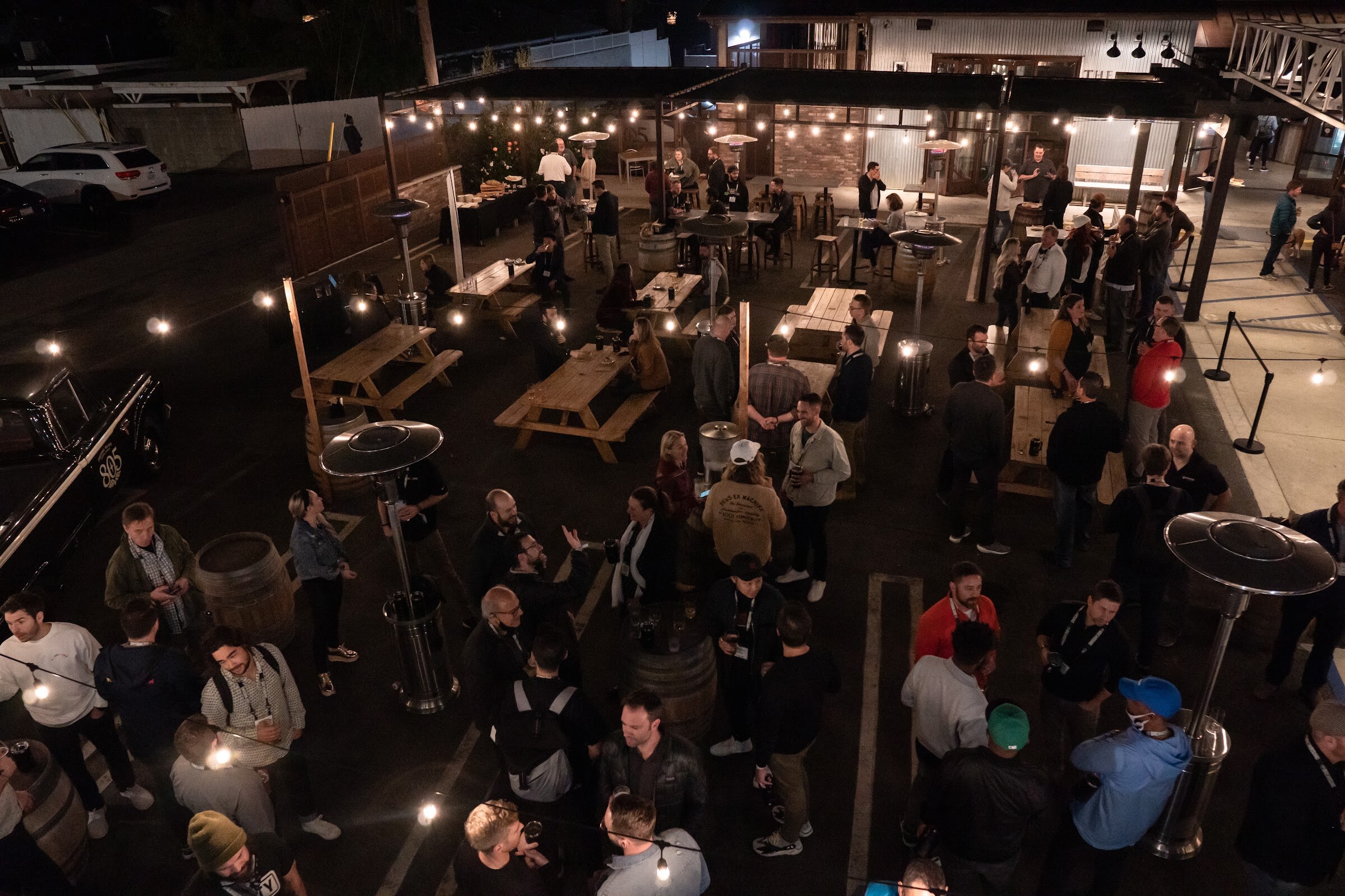 An elevated wide view of a courtyard at night filled with attendees standing among tables and string lights.