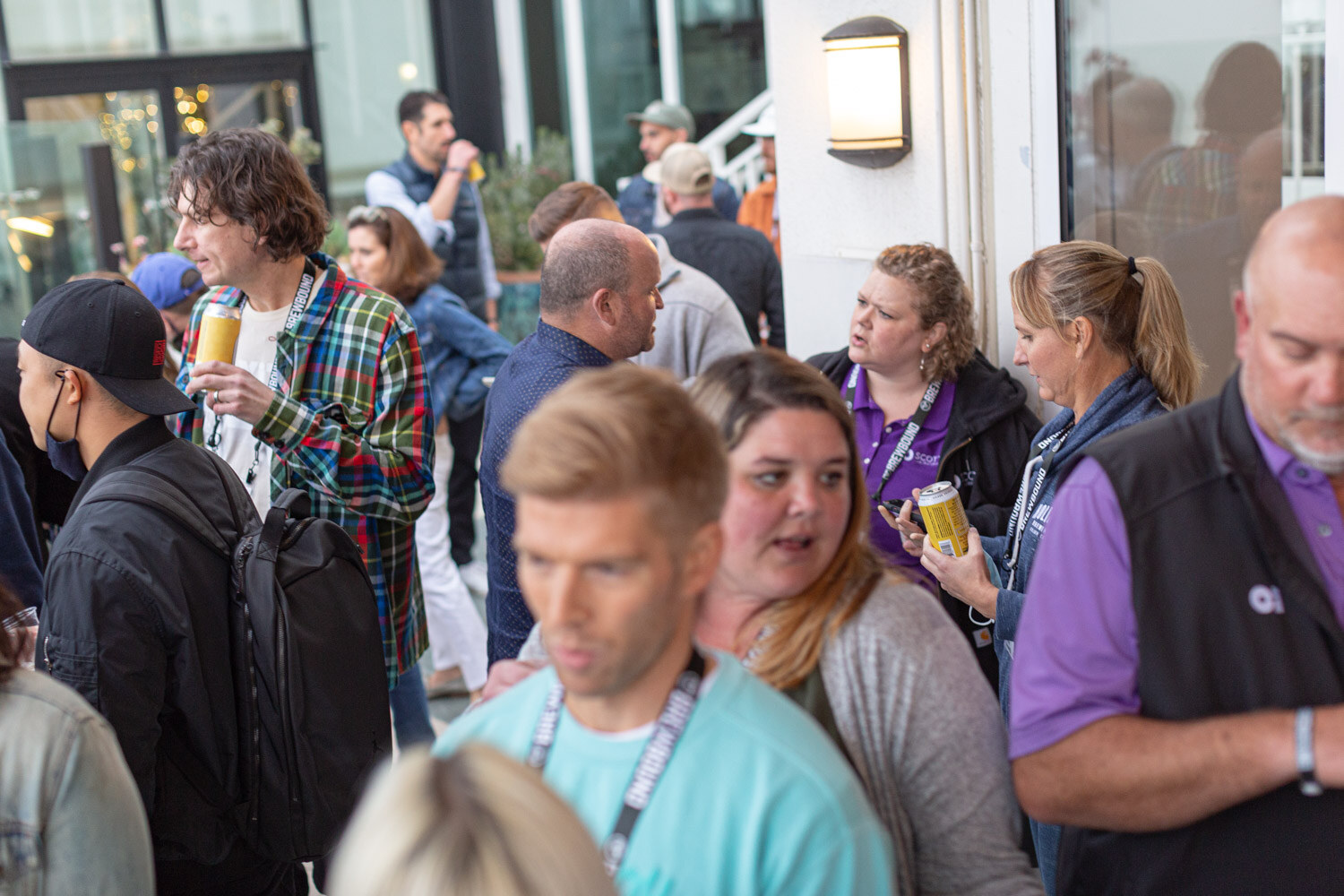 A crowd of attendees talking and holding cans on a terrace at the Wrap Party.