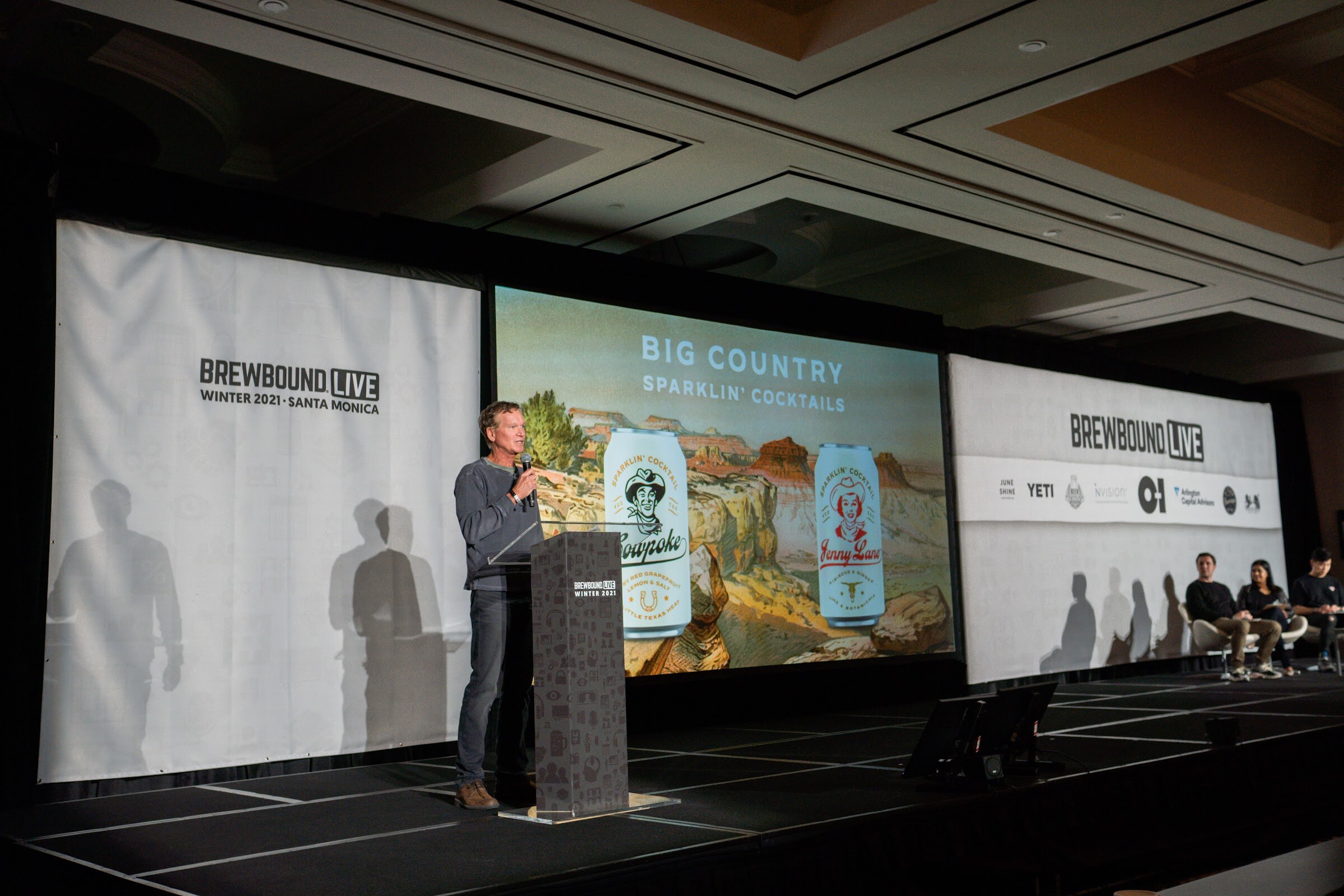 A man speaks at the podium on the Brewbound Live stage in front of a screen showing Big Country Sparklin' Cocktails cans.