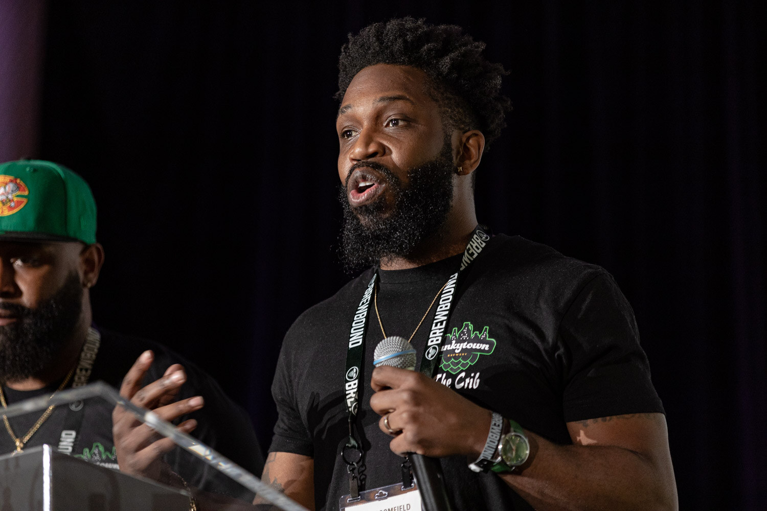 A bearded man in a Funkytown shirt speaks into a microphone as a teammate stands beside him.
