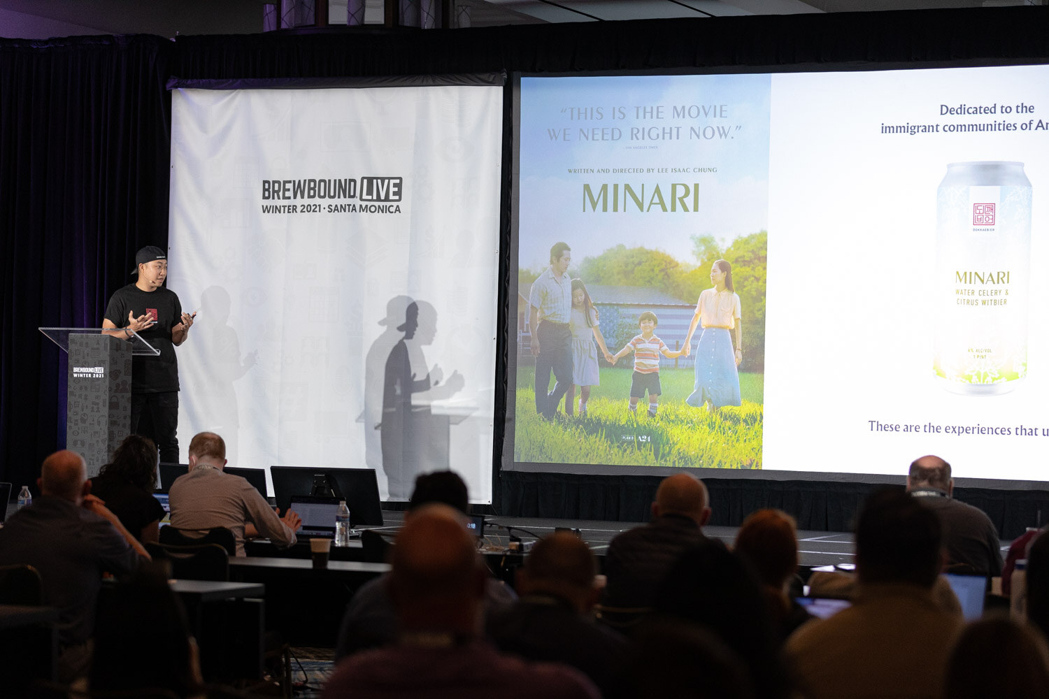 A man at a podium beside a large slide showing the Minari movie poster and a can of Minari beer.