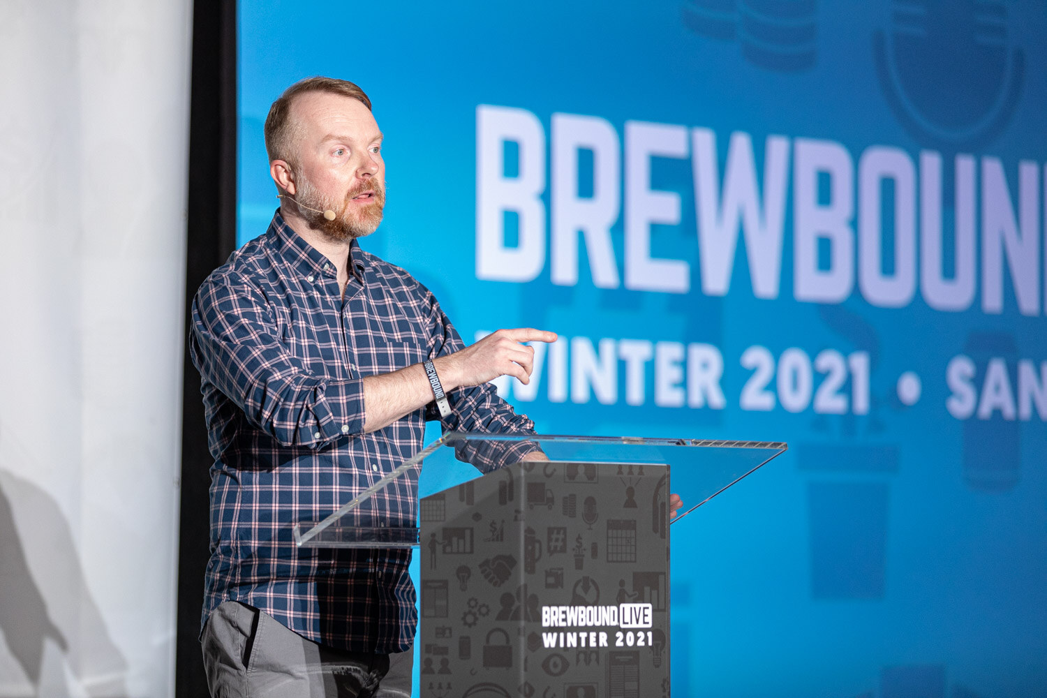 A bearded man in a plaid shirt speaks at a podium in front of a blue Brewbound Live Winter 2021 screen.