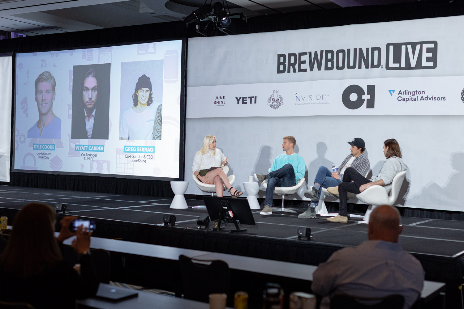 Four people sit on a stage in front of a Brewbound Live banner, with a screen at left showing three portrait photos with name captions.