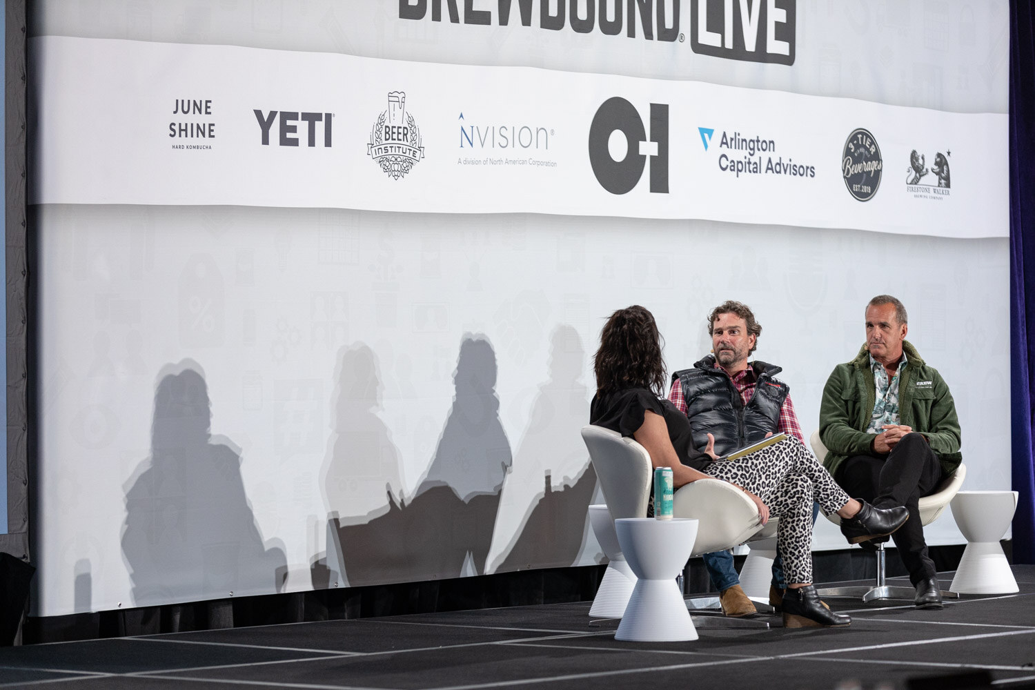 A wide view of three people seated on a stage under a banner with JuneShine, YETI, Beer Institute and O-I logos.