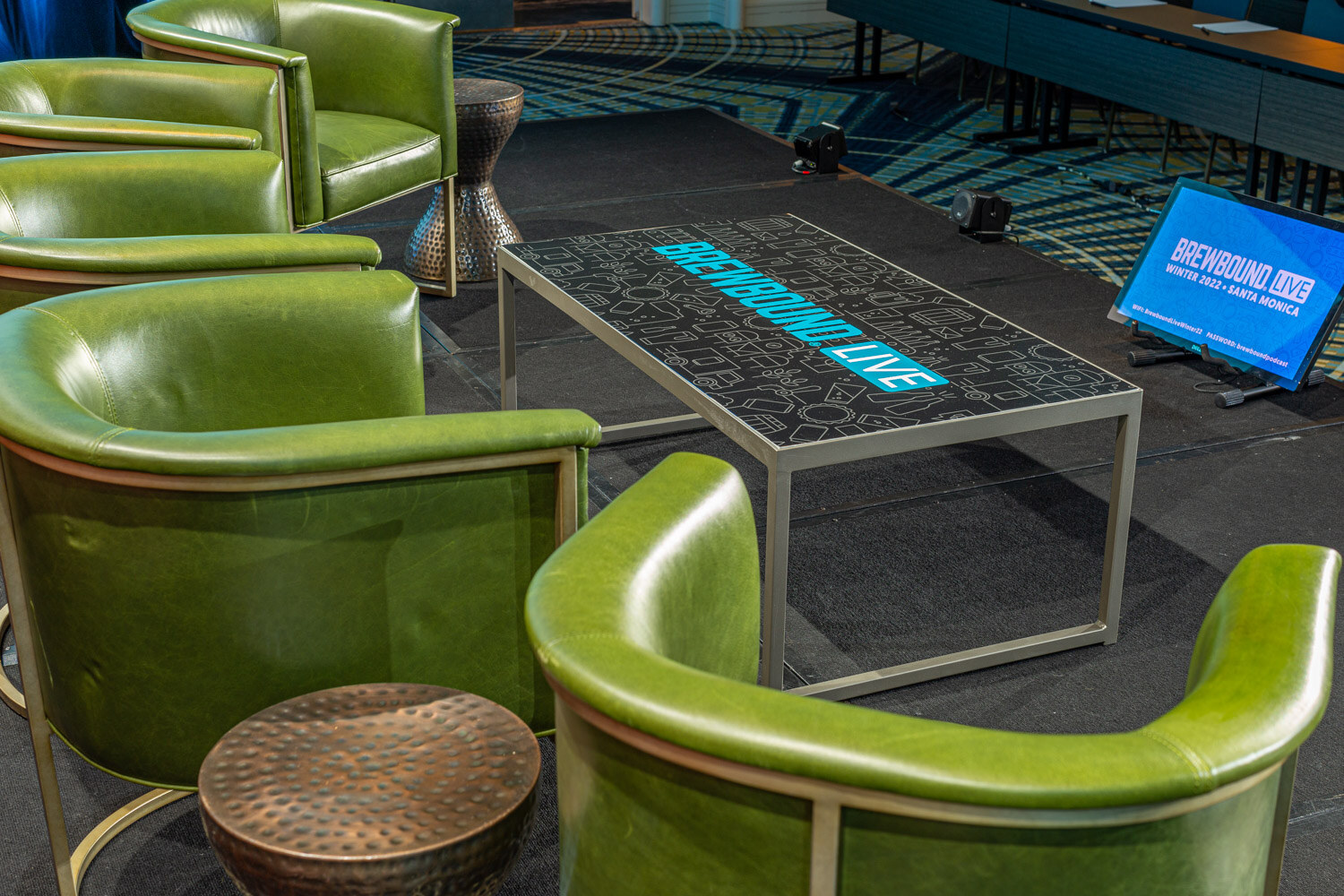 Close view of green leather armchairs around a glass coffee table with a glowing Brewbound Live logo.