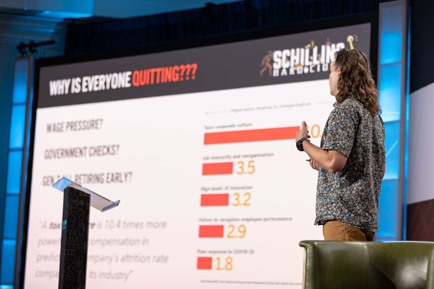A man in a patterned shirt stands beside a large screen showing a slide titled Why Is Everyone Quitting with a bar chart.