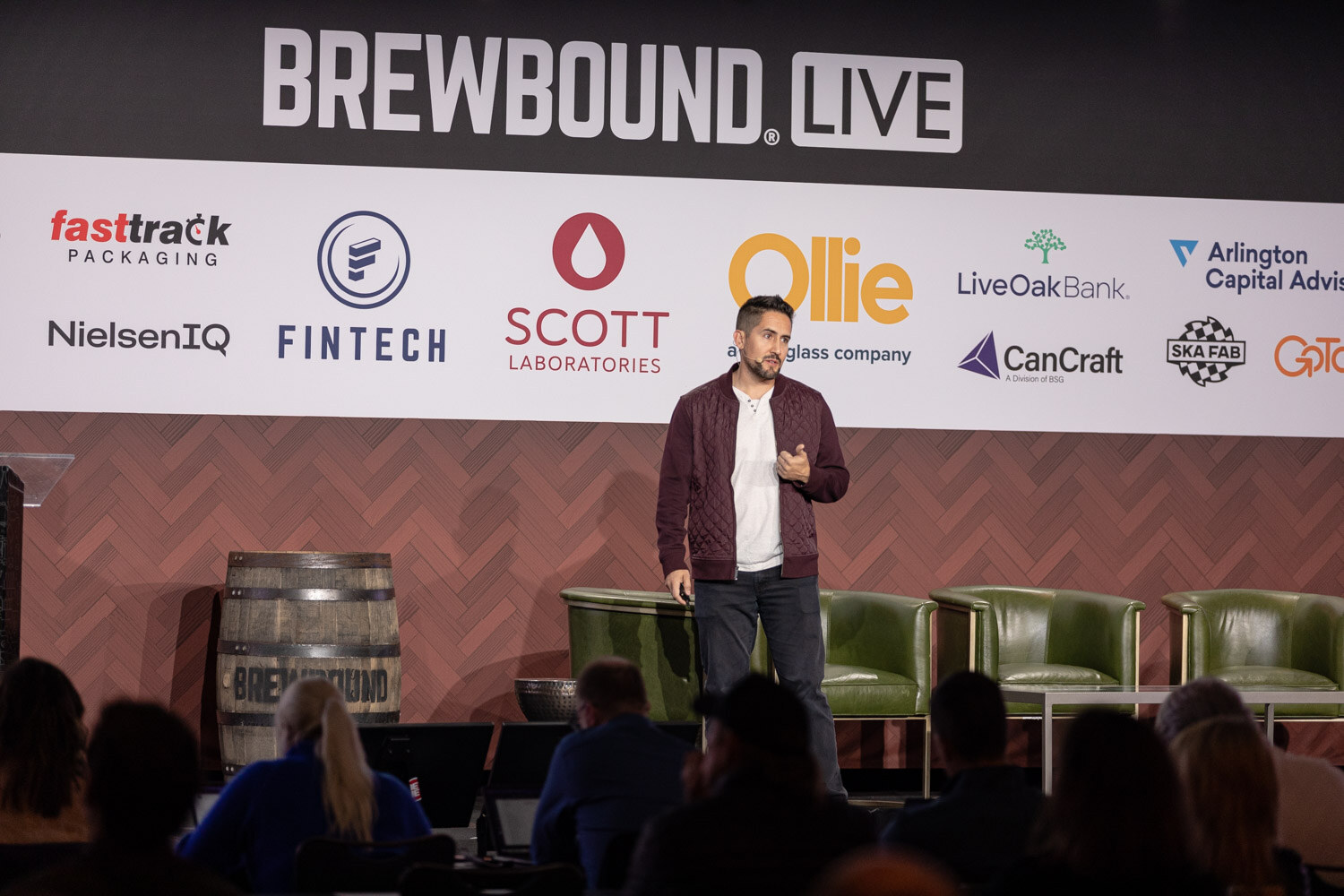 Wide view of a man in a maroon jacket on stage under the Brewbound Live banner with seated attendees in silhouette.