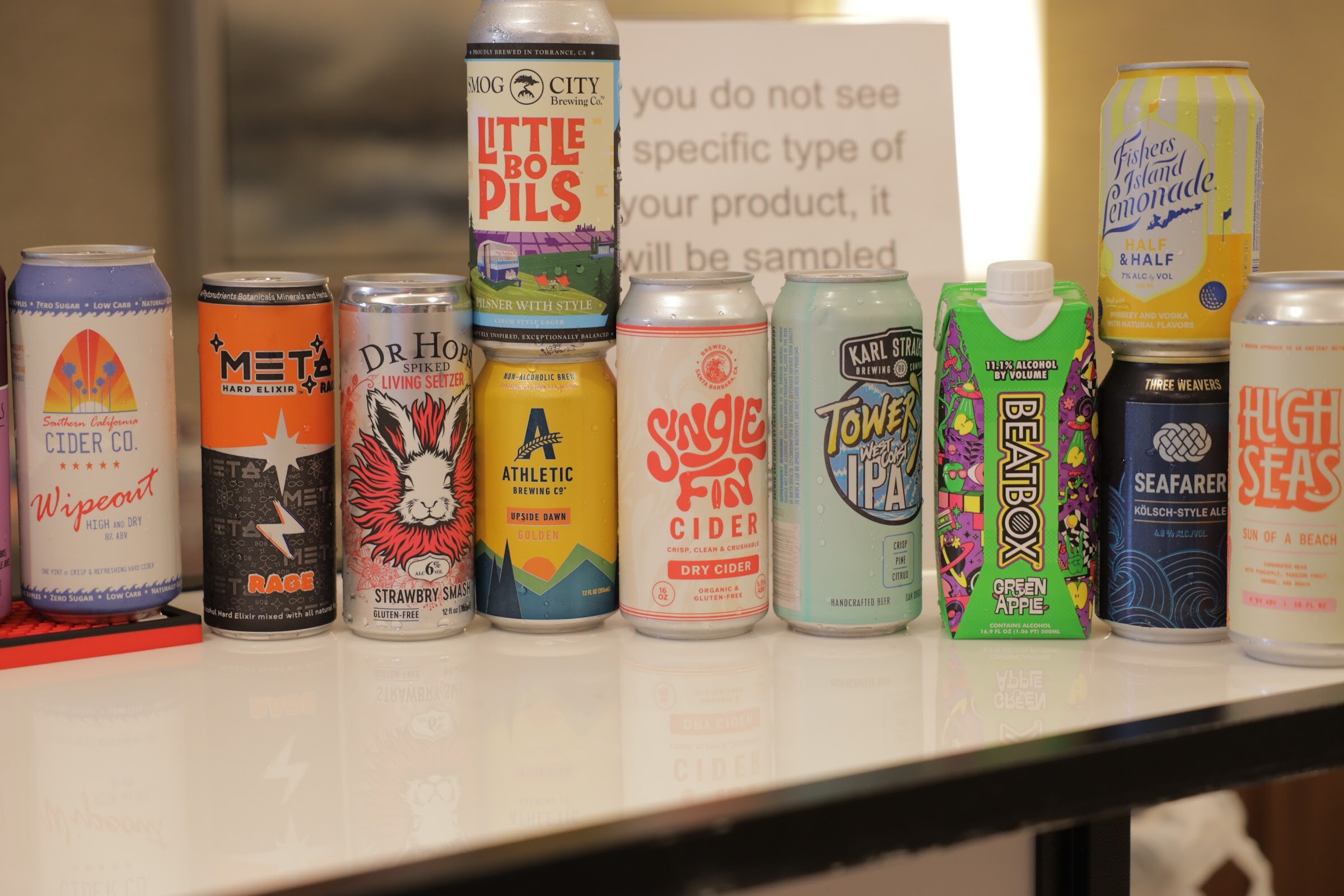 A white counter holds a row of cans including Wipeout cider, Rage, Little Pils, Athletic, Single Fin cider, BeatBox and Seafarer.