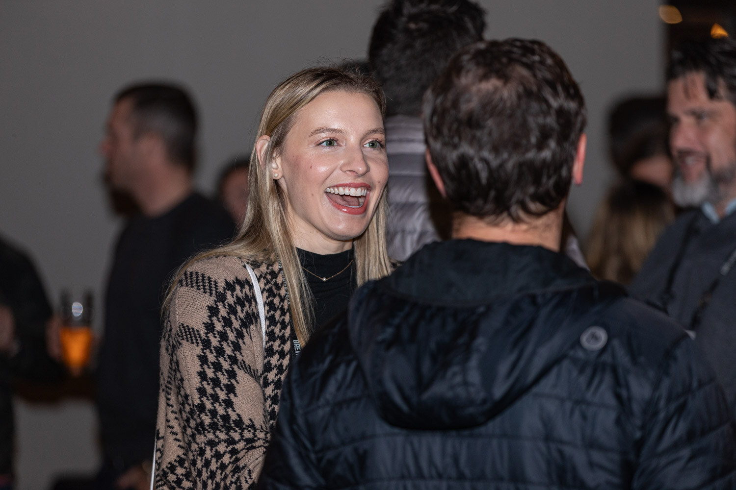 A woman with blonde hair laughs with her mouth open while talking to a man in a dark puffer jacket.