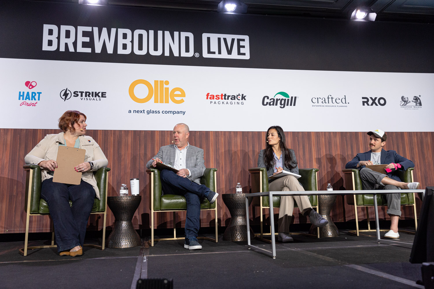 Four people sit in green armchairs on stage under the Brewbound Live banner, holding clipboards.