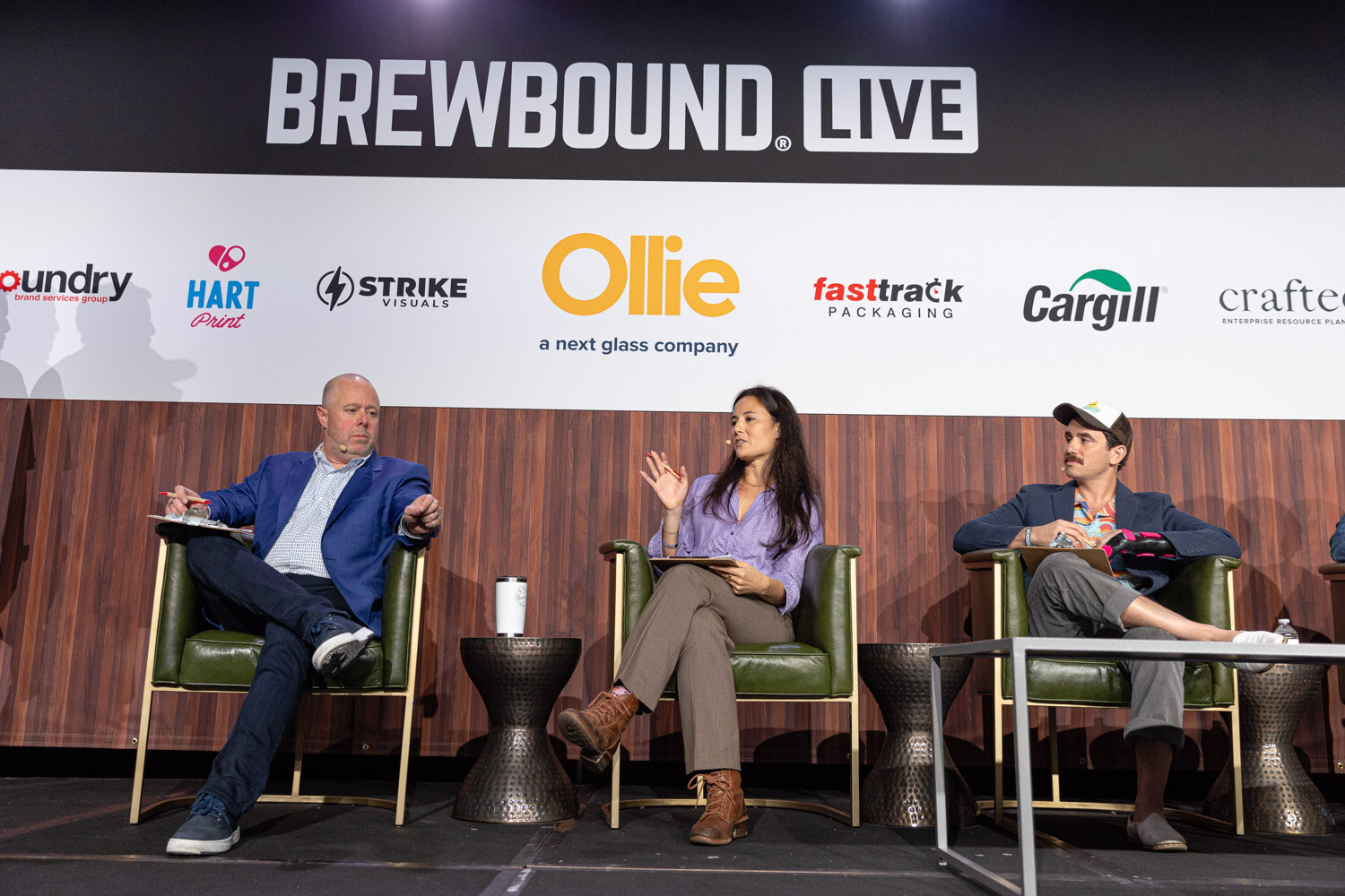 Two men and a woman sit in green armchairs under the Brewbound Live banner and sponsor logos.