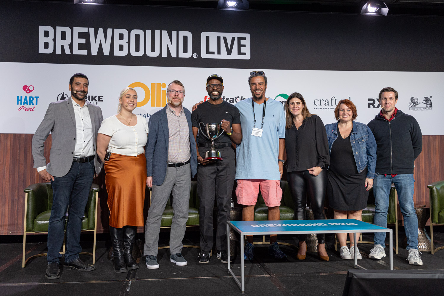 Nine people stand in a row on stage in front of the Brewbound Live backdrop, one holding a trophy.
