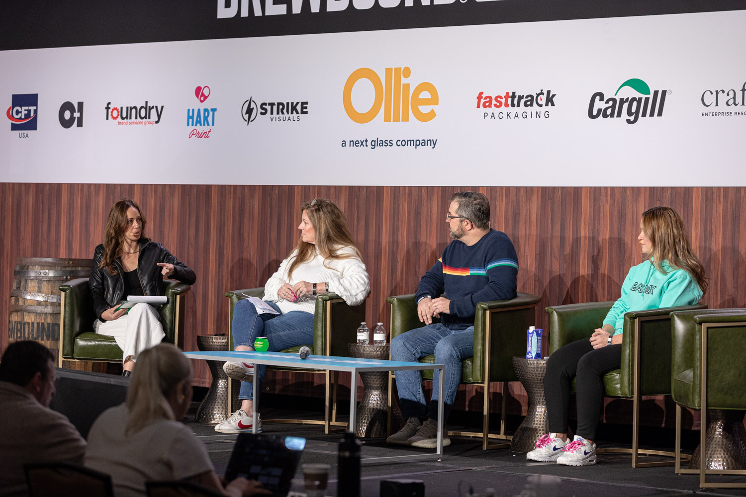 Four people sit in armchairs on a stage in front of a sponsor banner, one wearing a teal BeatBox hoodie.