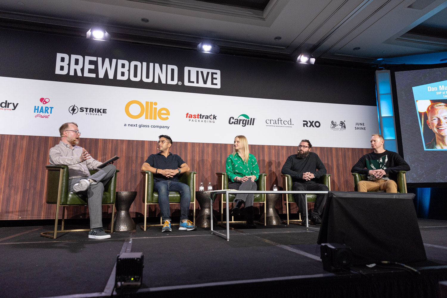 Five people sit in green armchairs on a stage under the Brewbound Live banner while a screen shows a speaker's photo.