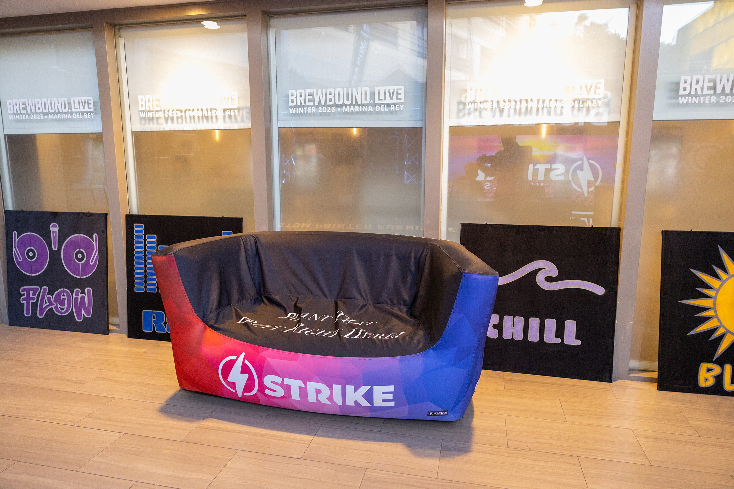 A blue, red and black inflatable couch with a Strike logo sits in a hallway in front of Brewbound Live signs.