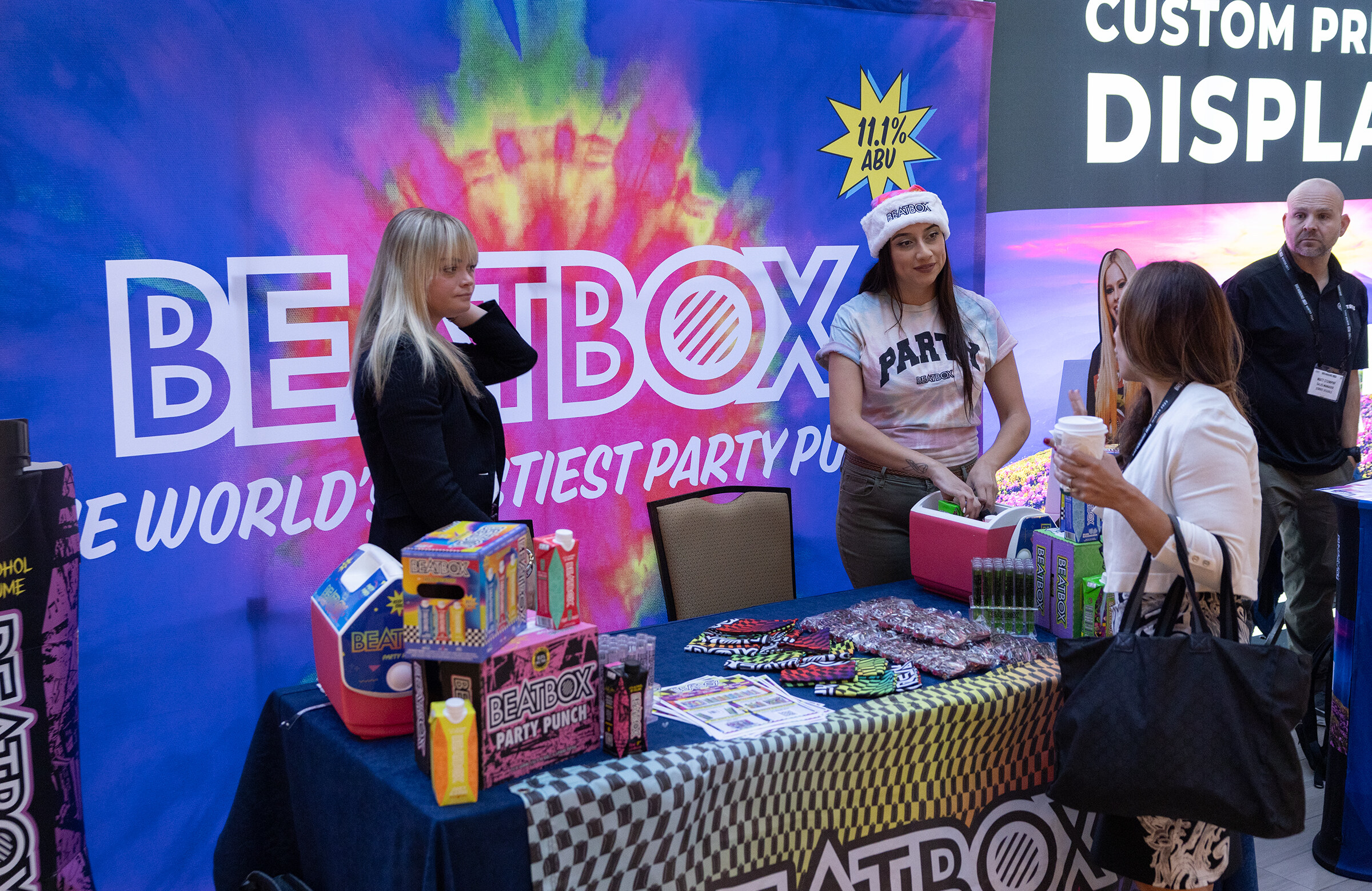 A woman in a white cap works at a table with party-themed items in front of a colorful BeatBox backdrop.