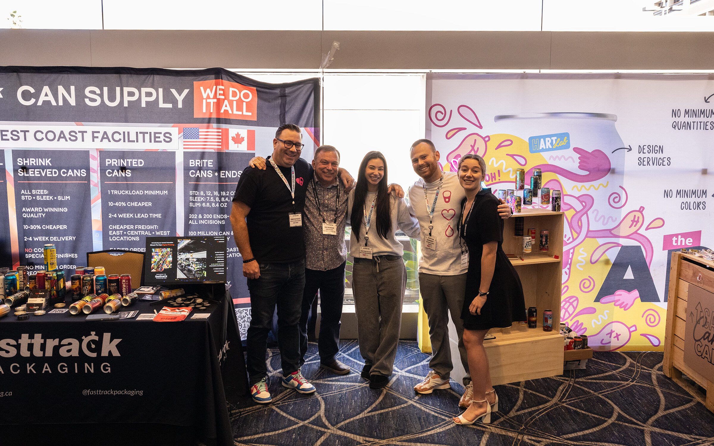 Six people stand arm in arm in front of the Fasttrack Packaging and Hart Print displays.