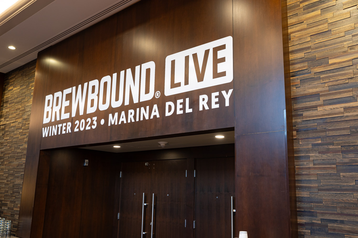 A dark wood wall with a Brewbound Live Winter 2023 Marina del Rey sign above a pair of tall doors.