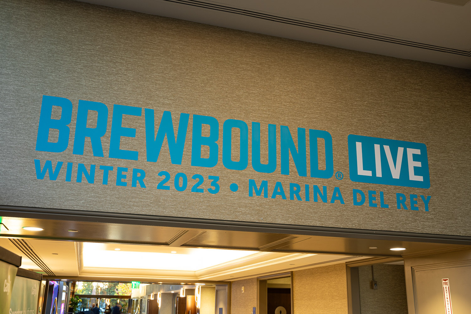 A teal Brewbound Live Winter 2023 Marina del Rey sign on a beige wall above a hallway.