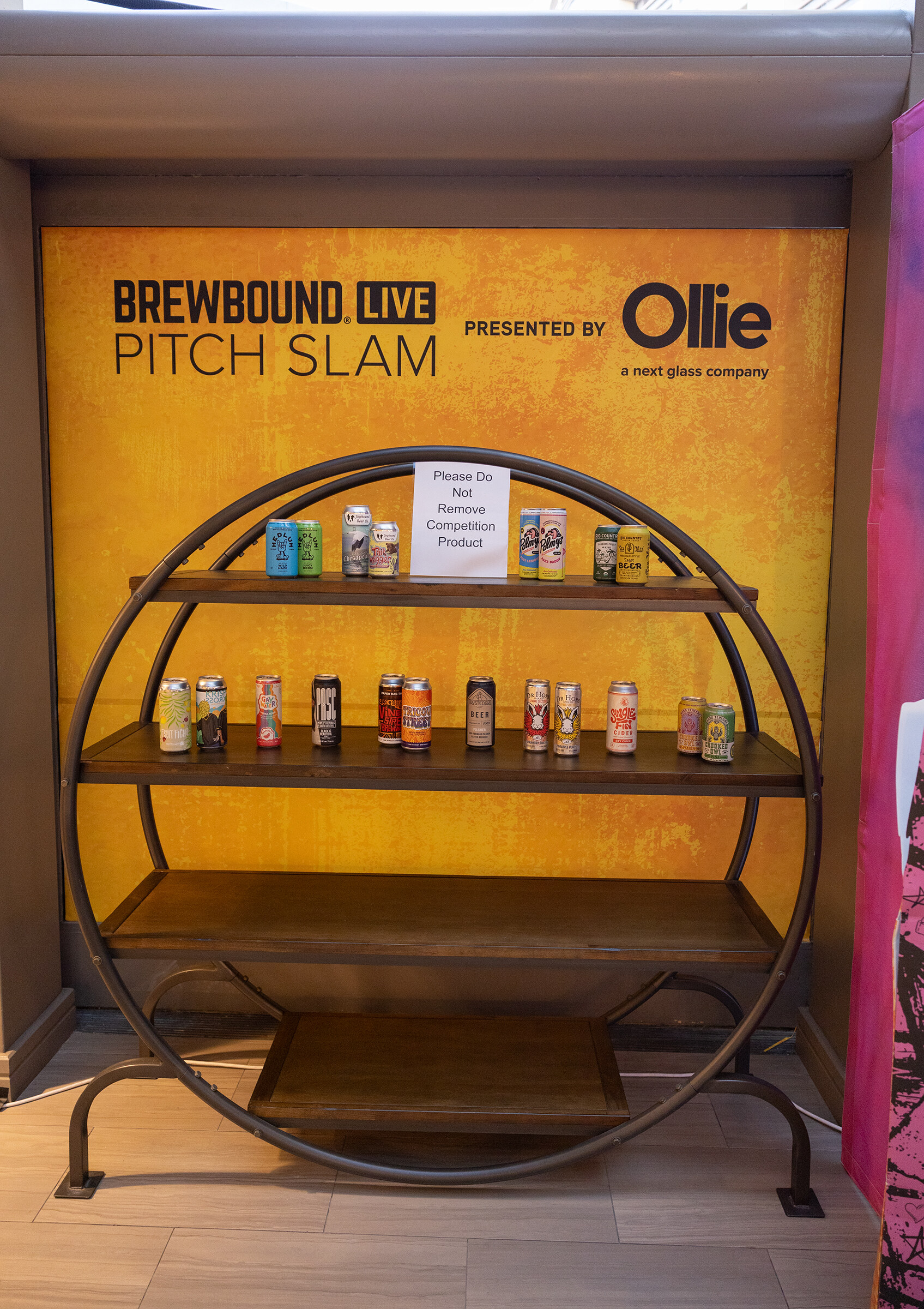 A circular shelf holding small cans in front of a yellow Brewbound Live Pitch Slam backdrop presented by Ollie.