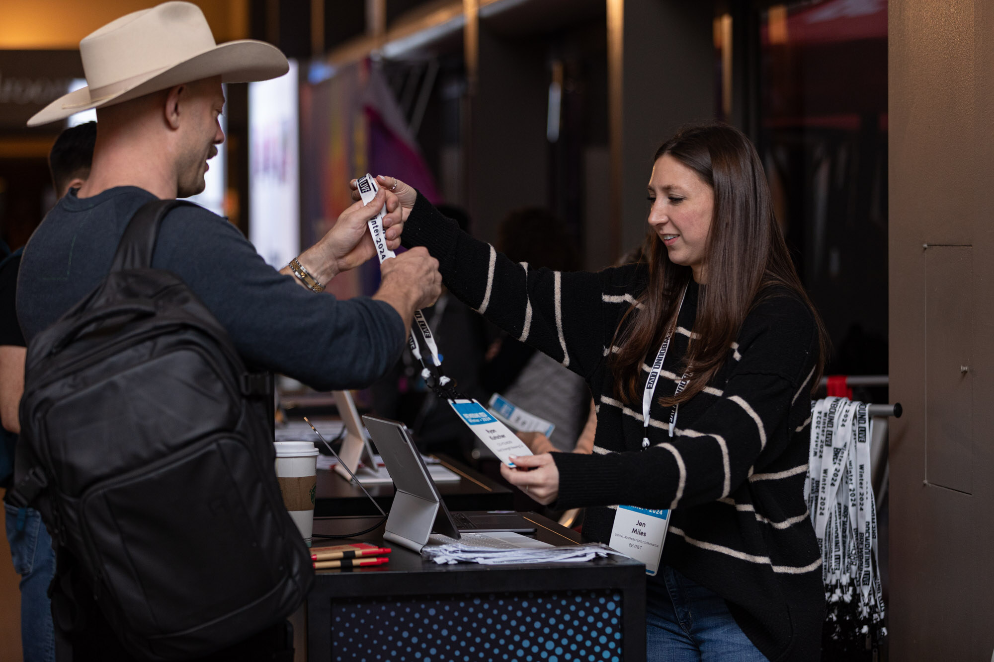 A man in a cowboy hat takes a lanyard from a woman at the registration desk.