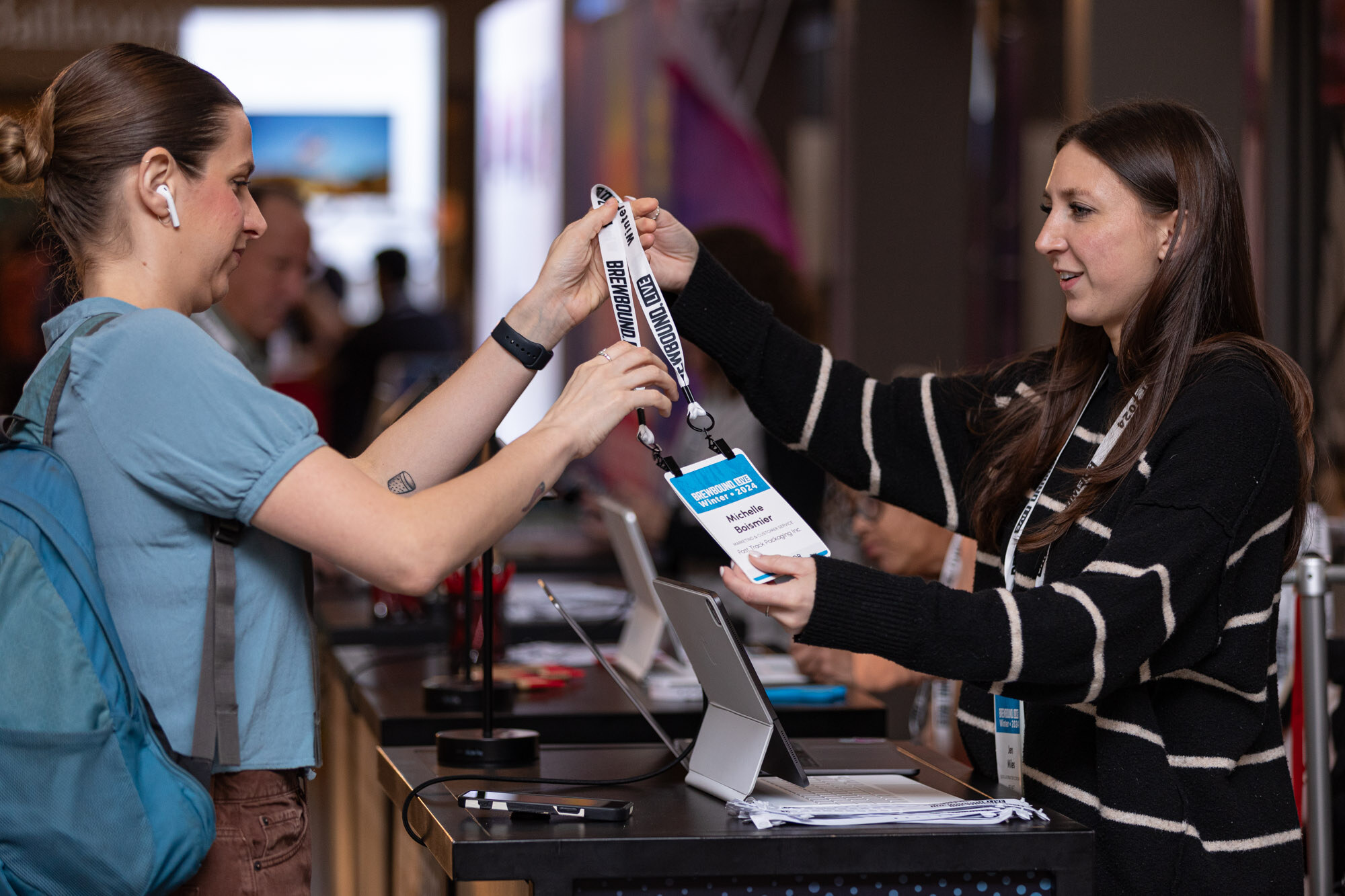 A woman hands a badge and lanyard across the registration desk to an attendee.