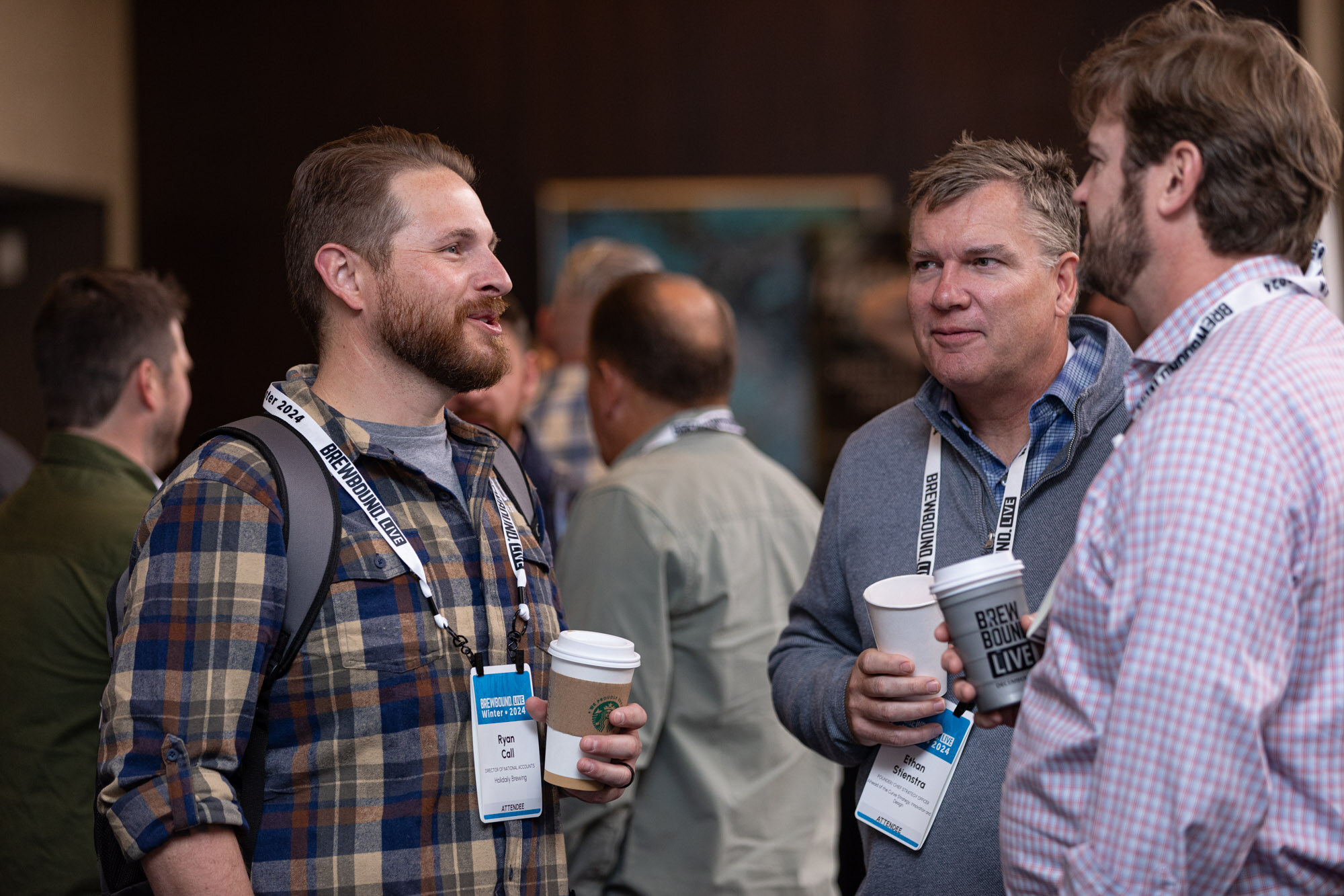 Three men with badges and coffee cups stand talking.