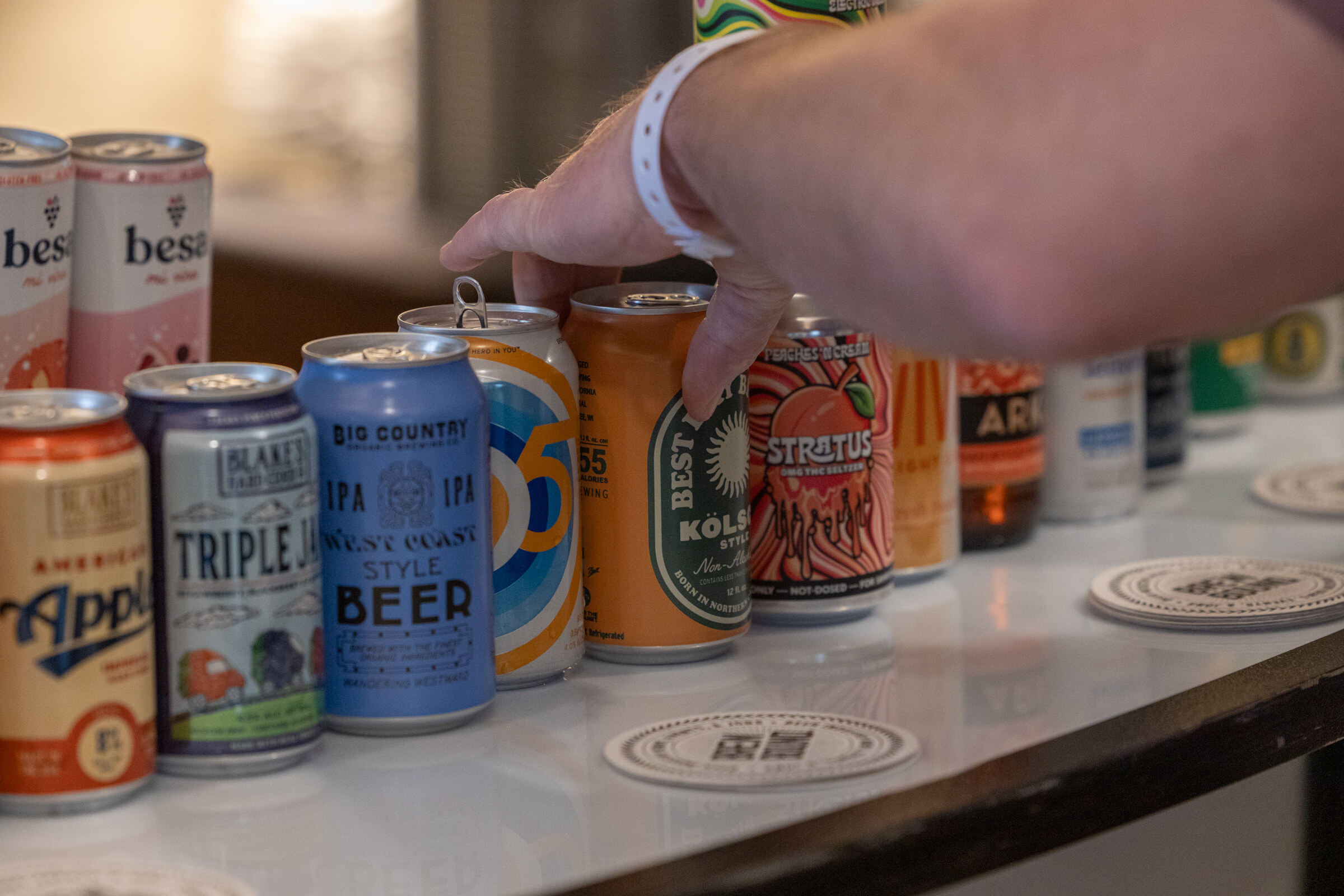 A hand with a wristband reaches toward a row of cans including besa and Big Country.