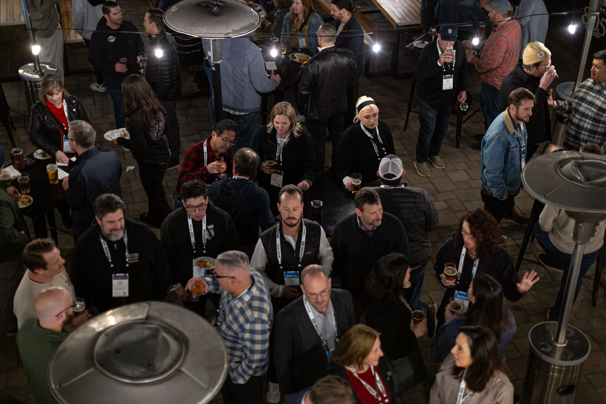 An overhead view of attendees with badges standing among patio heaters.