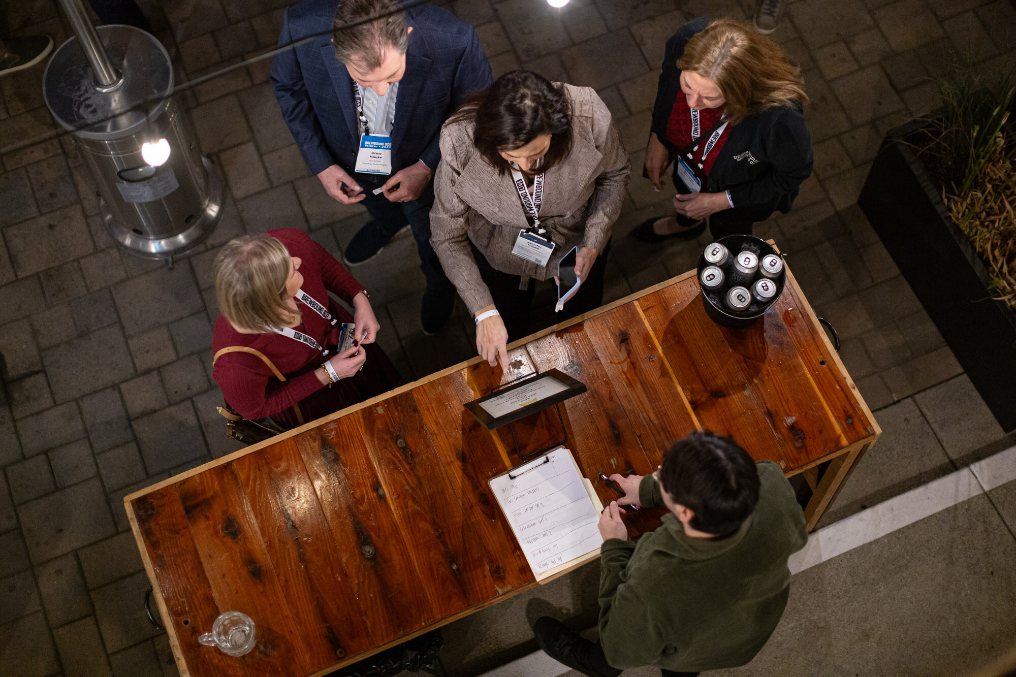 An overhead view of people with badges standing at a wooden table with a tablet and papers.