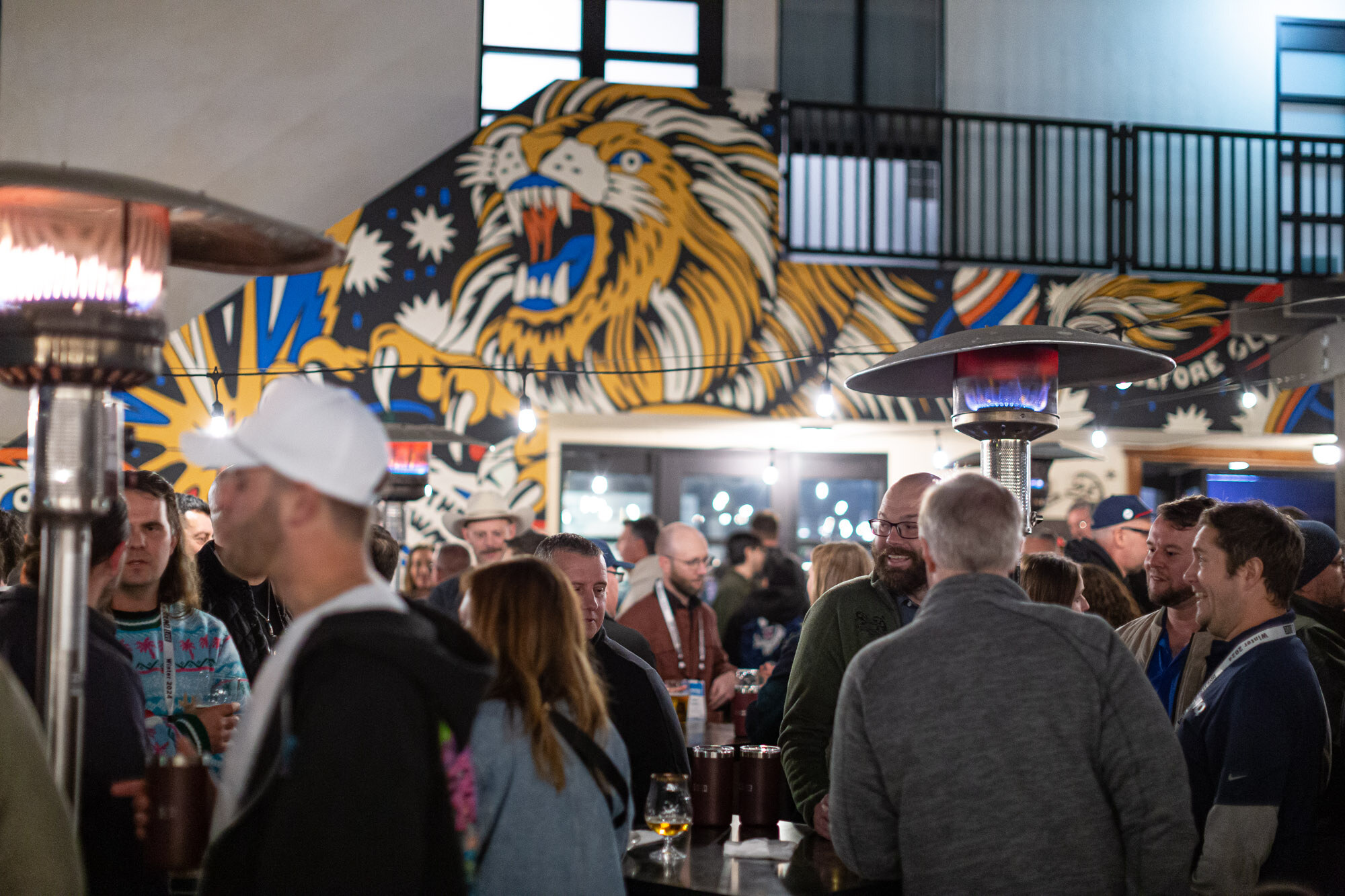 Attendees stand under a large lion mural on the patio wall at night.