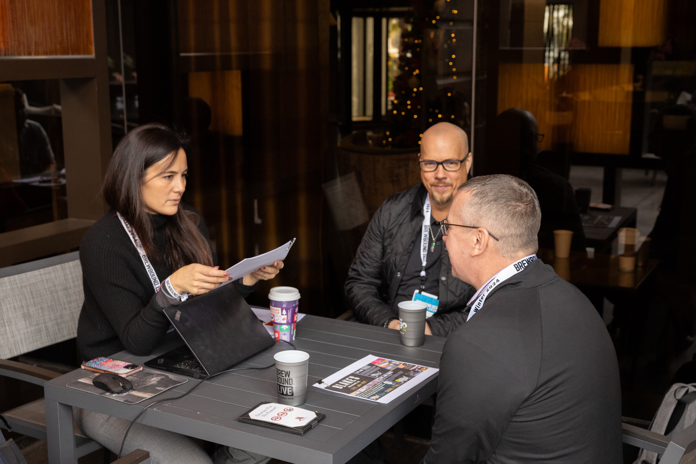 Two women and a man sit at a table with a laptop and papers.